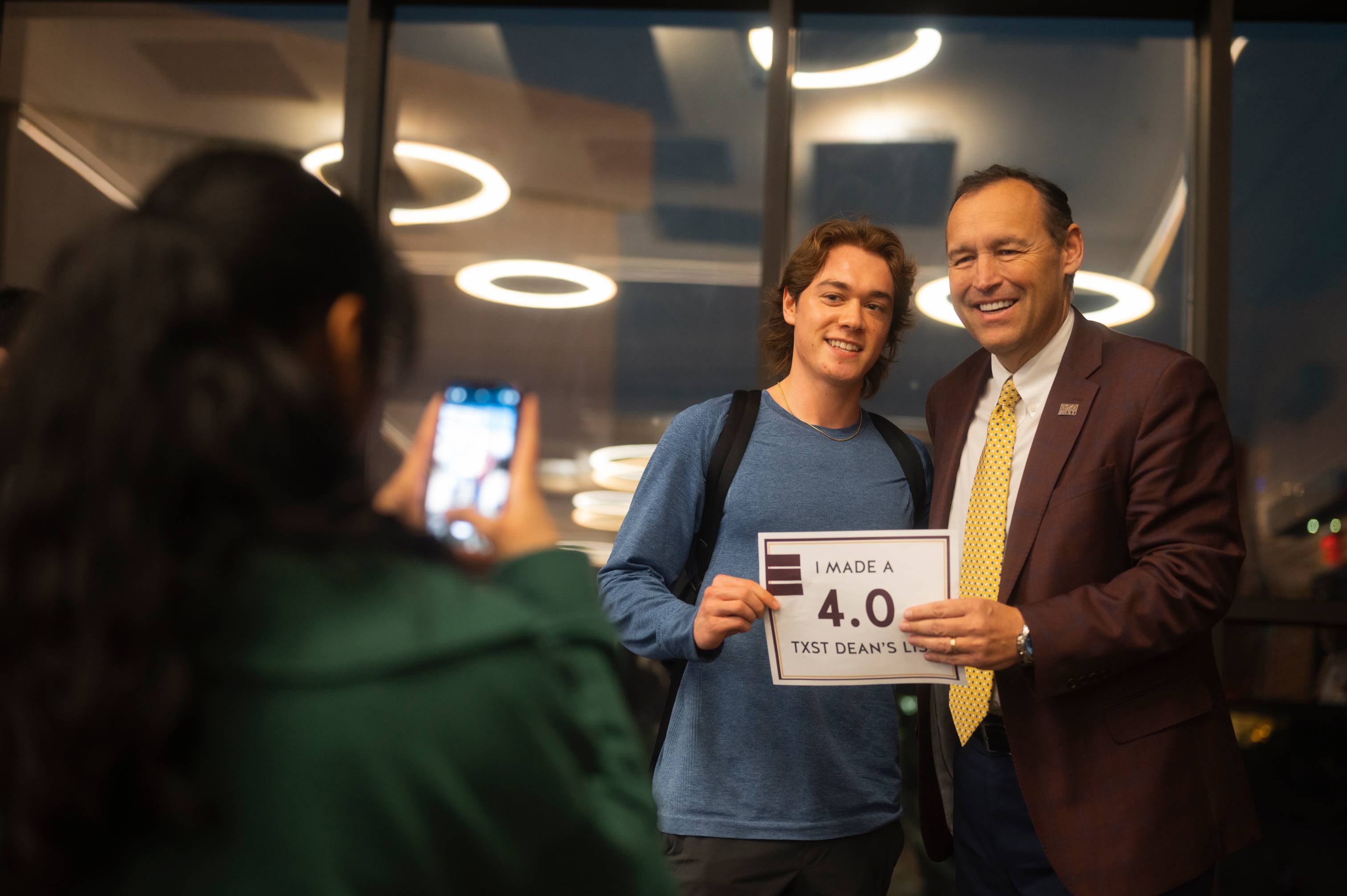 Student holding a sign that says "I got a 4.0" and posing with President Kelly Damphousse.