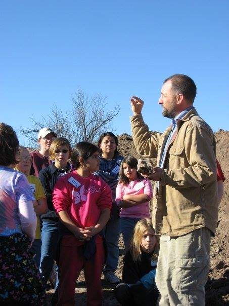 Archaeologist holding up an artifact in front of a group at an archaeological site