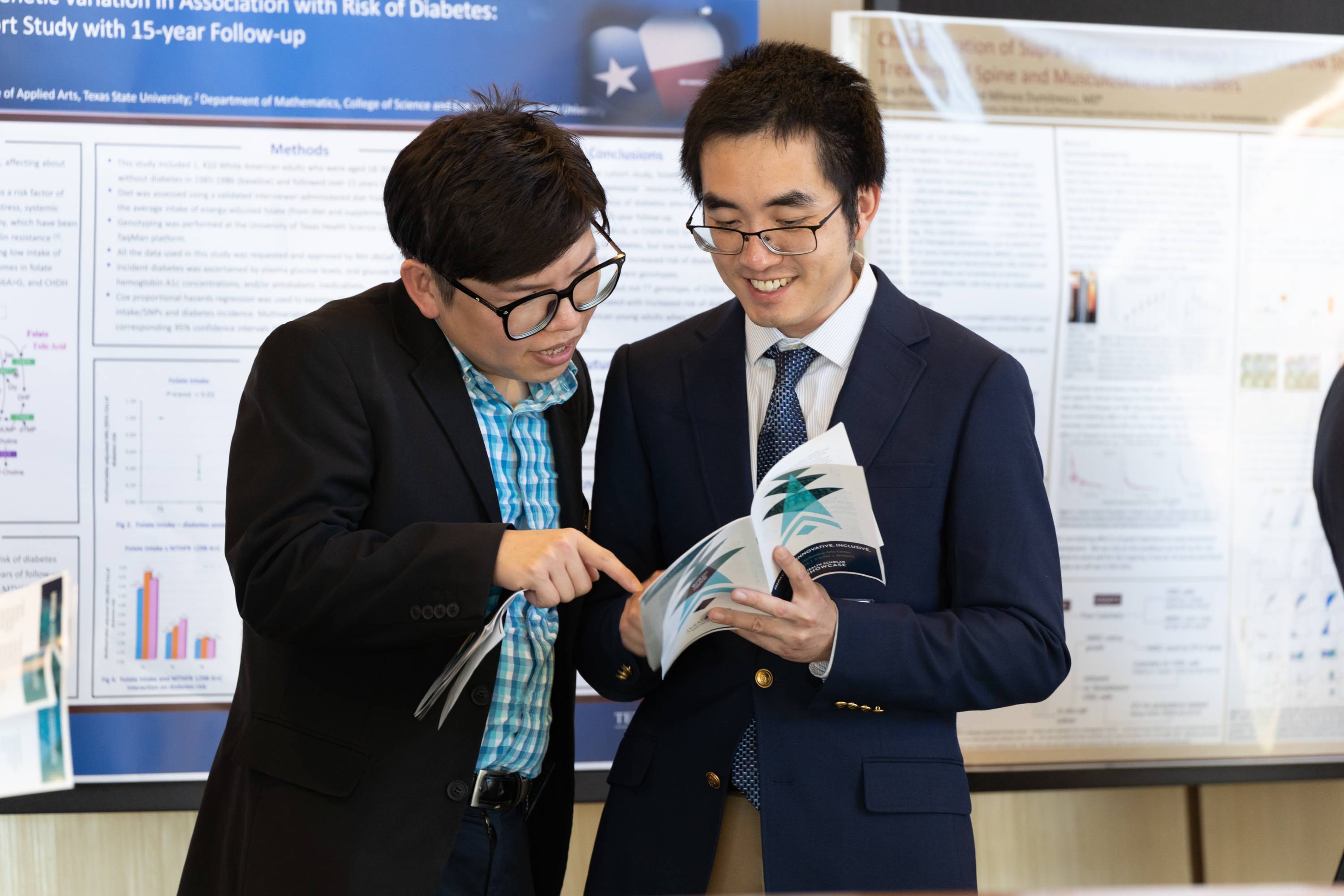 Two Showcase attendees look at the event brochure. Two health research posters can be seen behind them.
