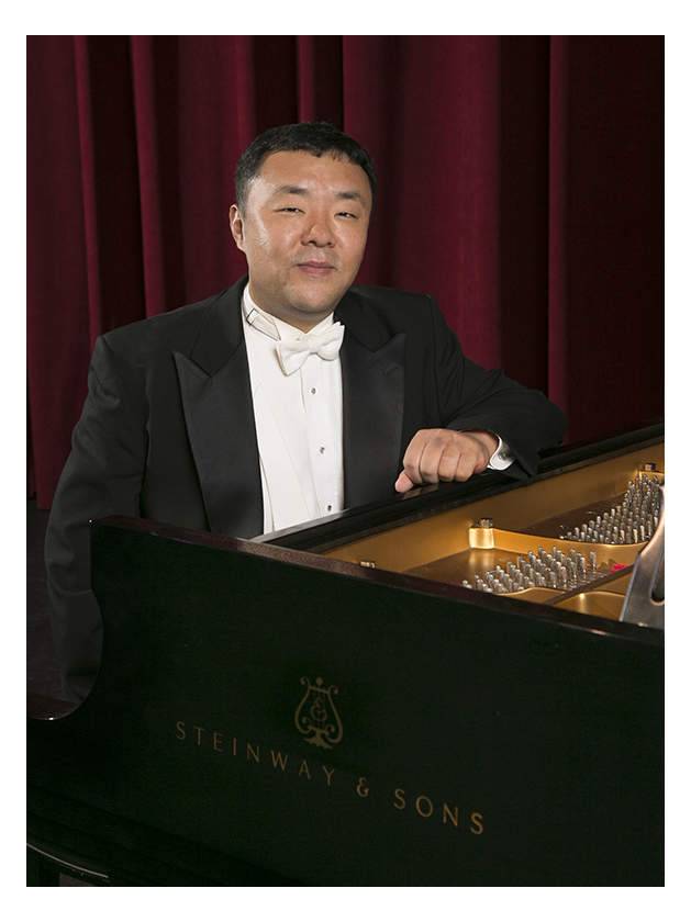 Portrait of Jason Kwak in concert tux at a grand piano keyboard.