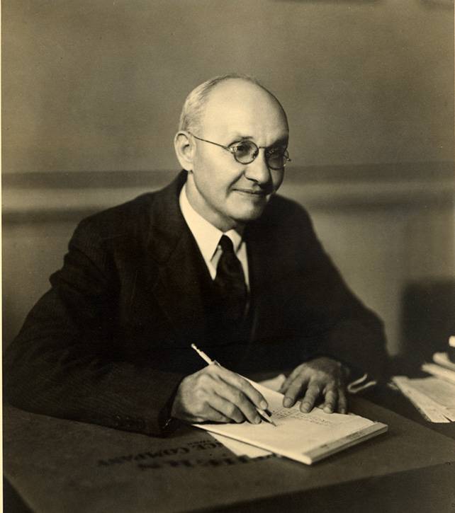 Photograph of President Evans writting at his desk.