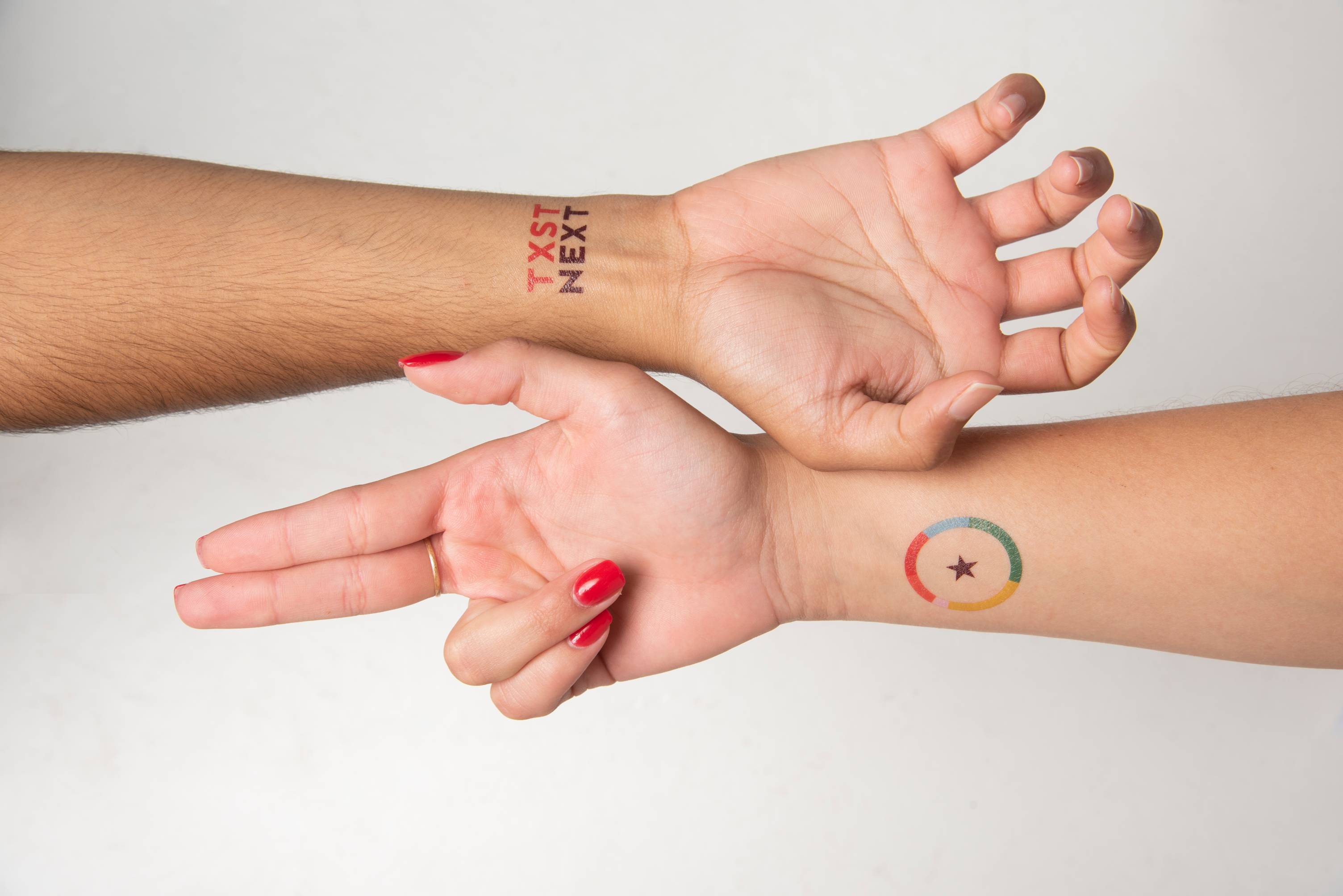 Two hands doing Texas State hand signs have Next temporary tattoos on the inside of their wrists