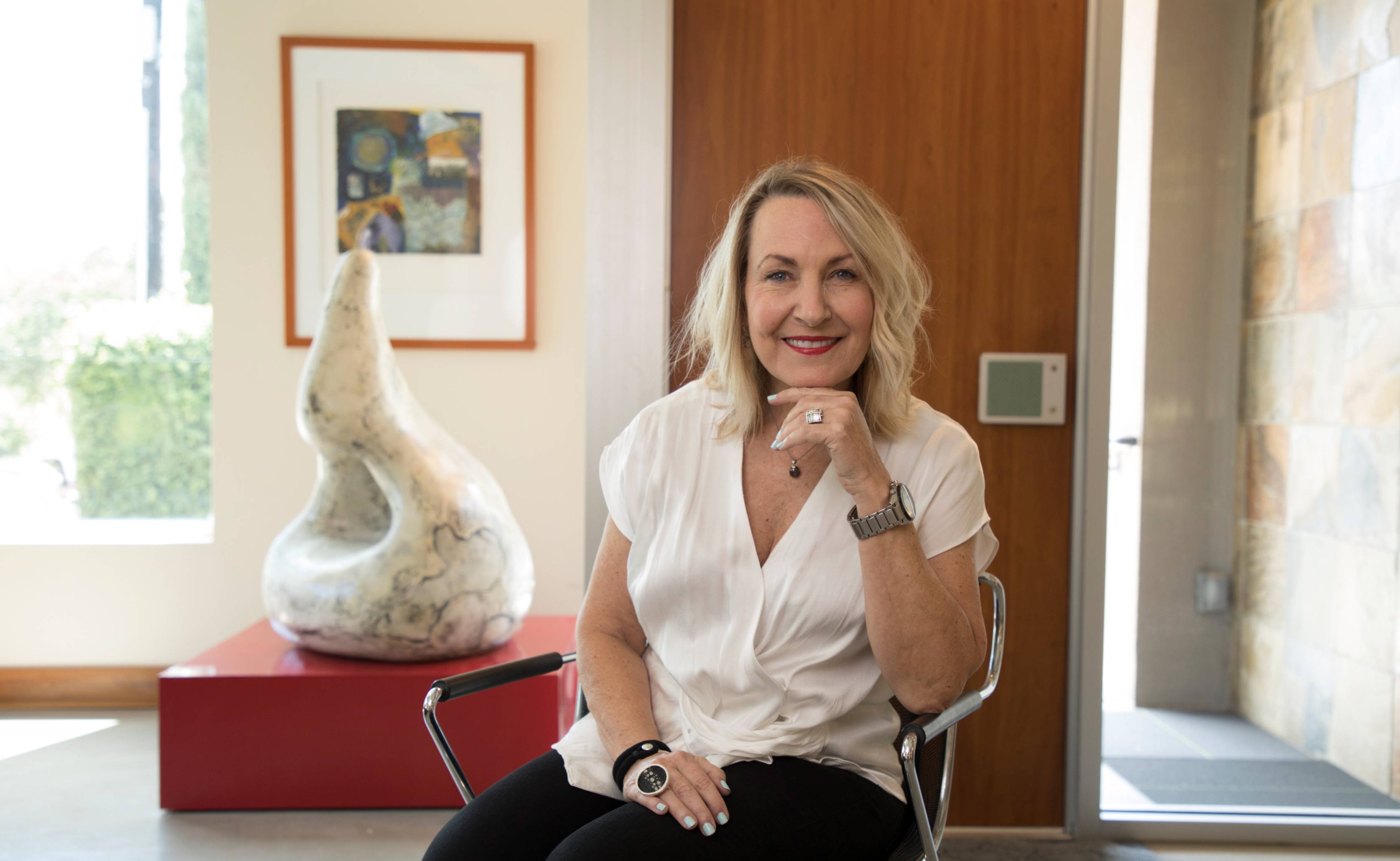 Donor, Leslie Fossler is seated in her office with a sclupture behind her
