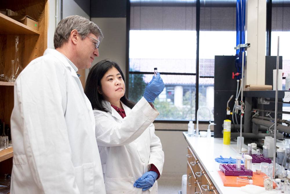 A photo of a professor and a student looking at a vial in a laboratory.