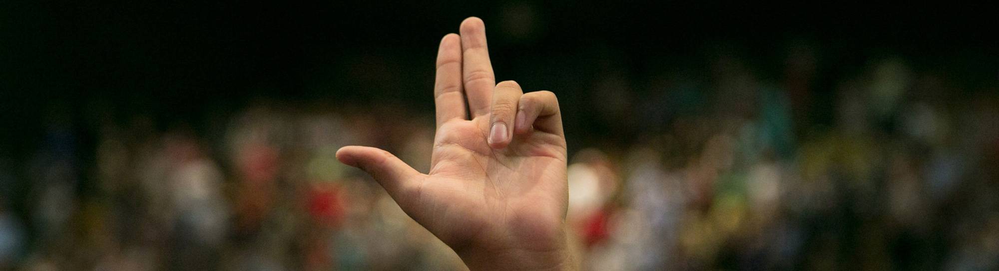 A Texas State grad's left hand in the air, holding their first two fingers and thumb out to form the shape of Texas.
