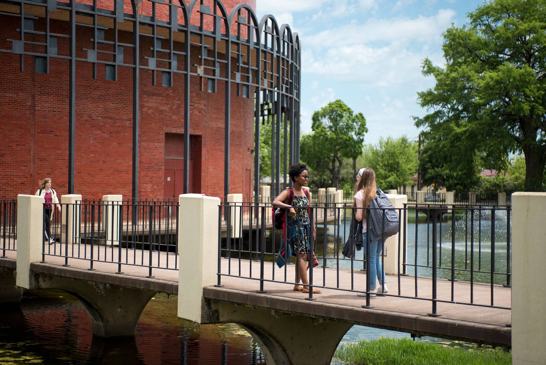 Texas State students pause to chat on the bridge leading to the iconic Theater Center .