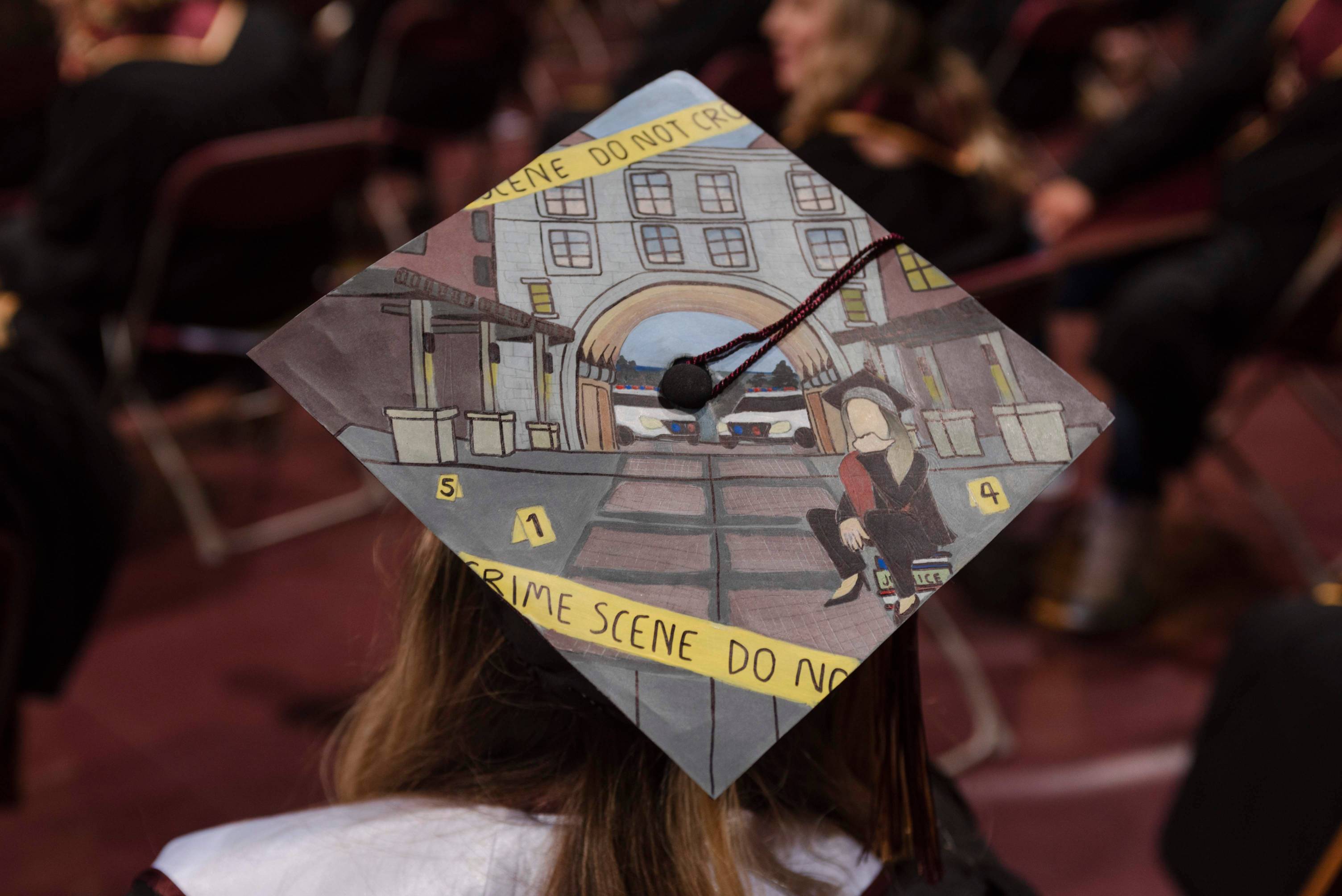 the back of a student's graduation cap is decorated in art of her as a graduate with crime scene tape