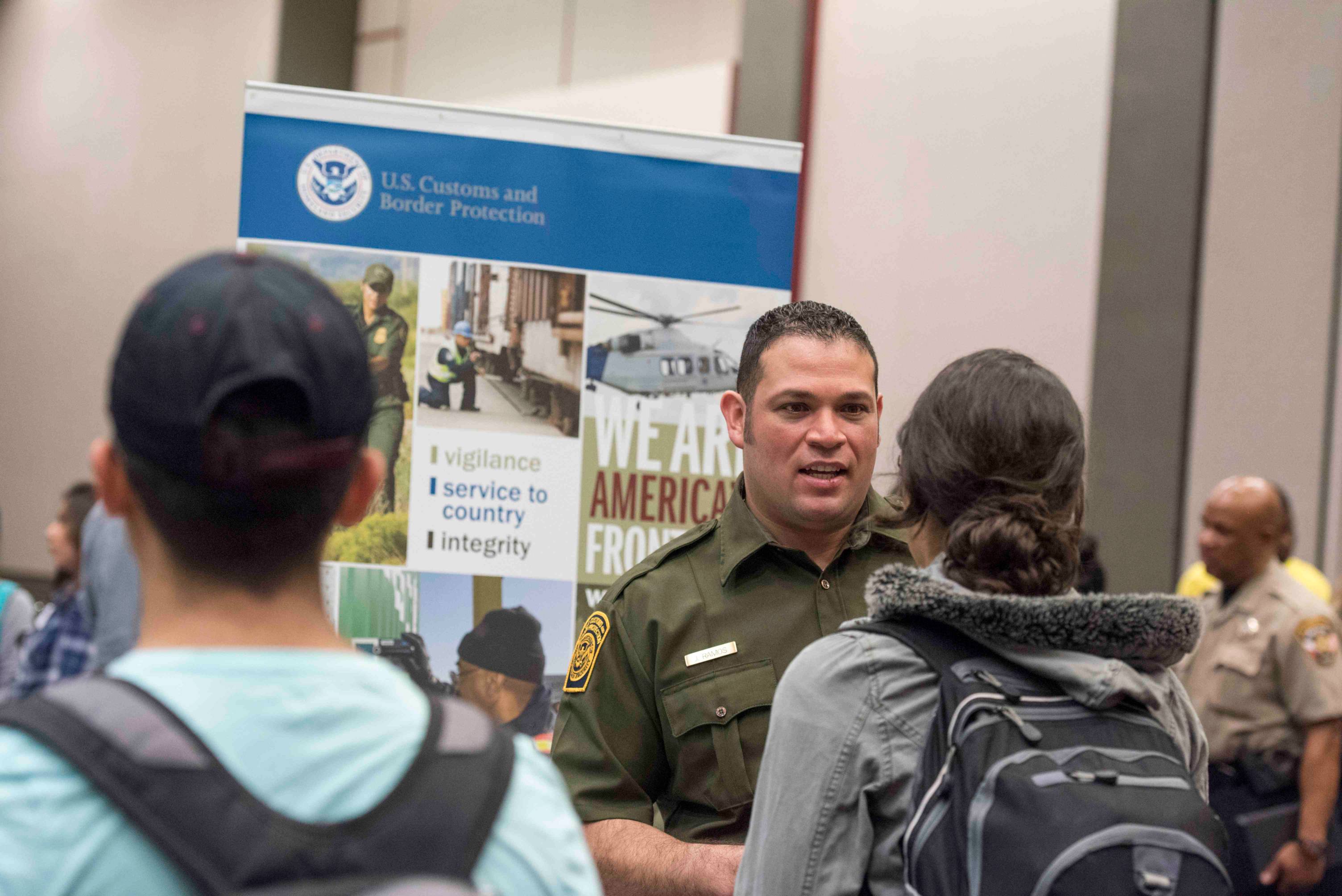 a border patrol officer speaks with two students during a career fair