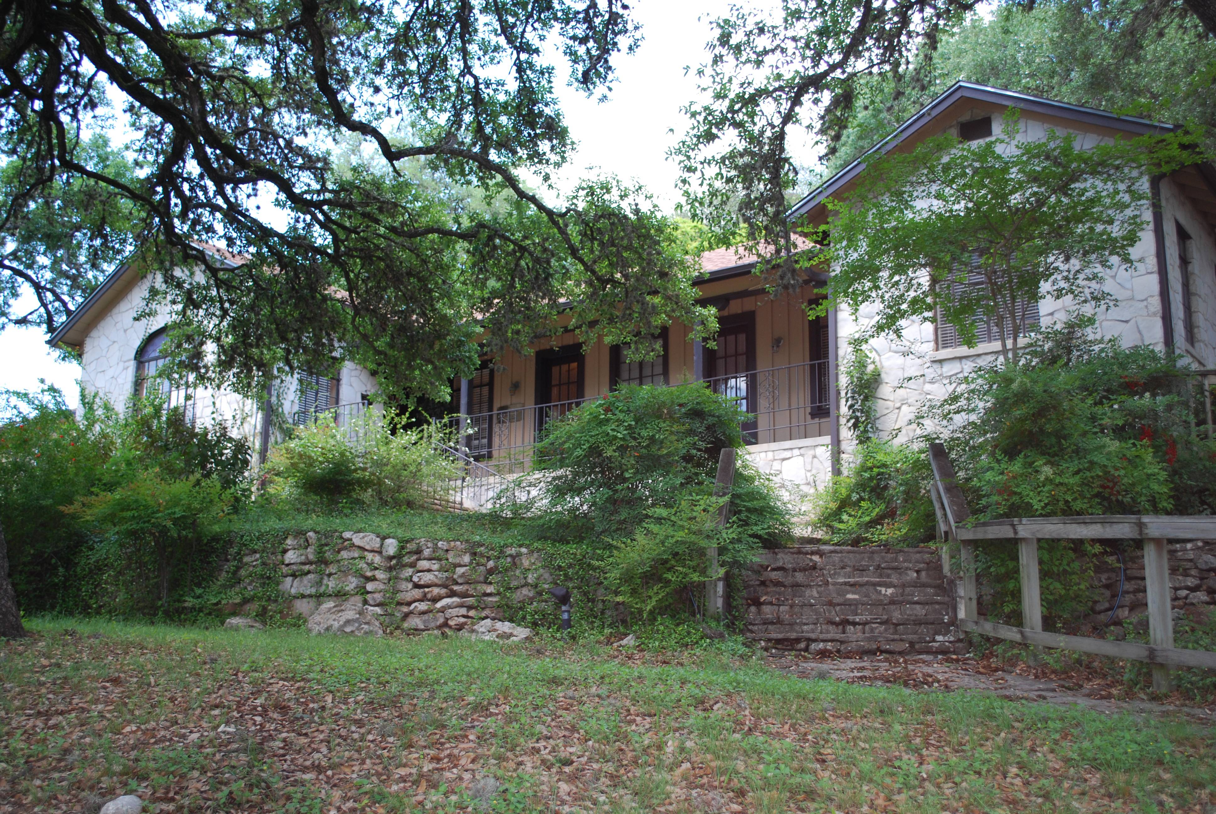 Small white brick building, known as The Smith House, with a small brick wall, stairs, and green vegetation out front