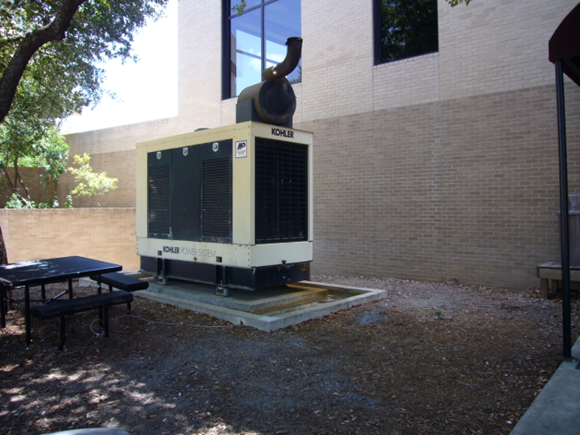 Generator stationed outside LBJSC and next to a tree and picnic table. 