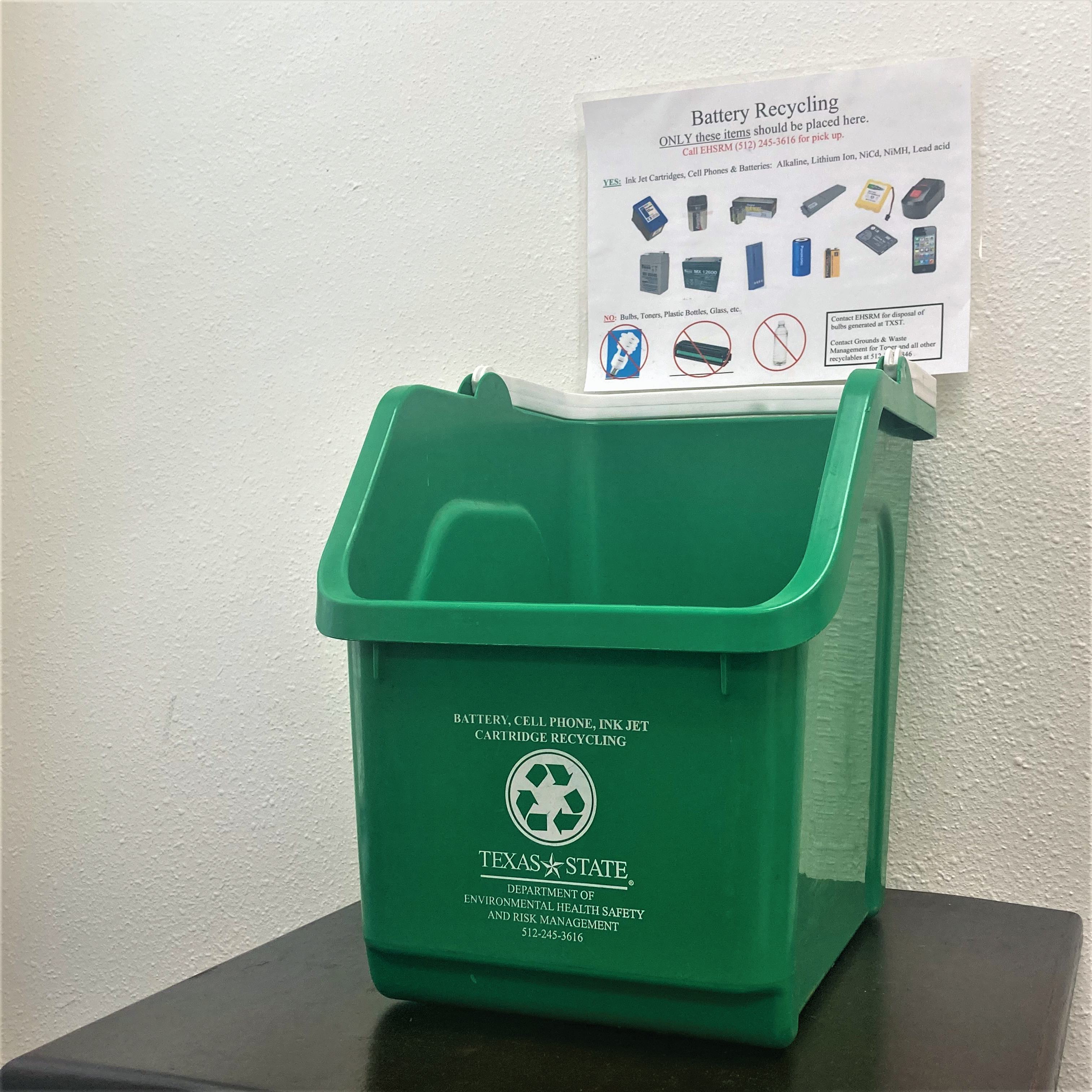 Green battery bin used to collect batteries, cell phones, and ink jets for recycling sits on a brown table. 