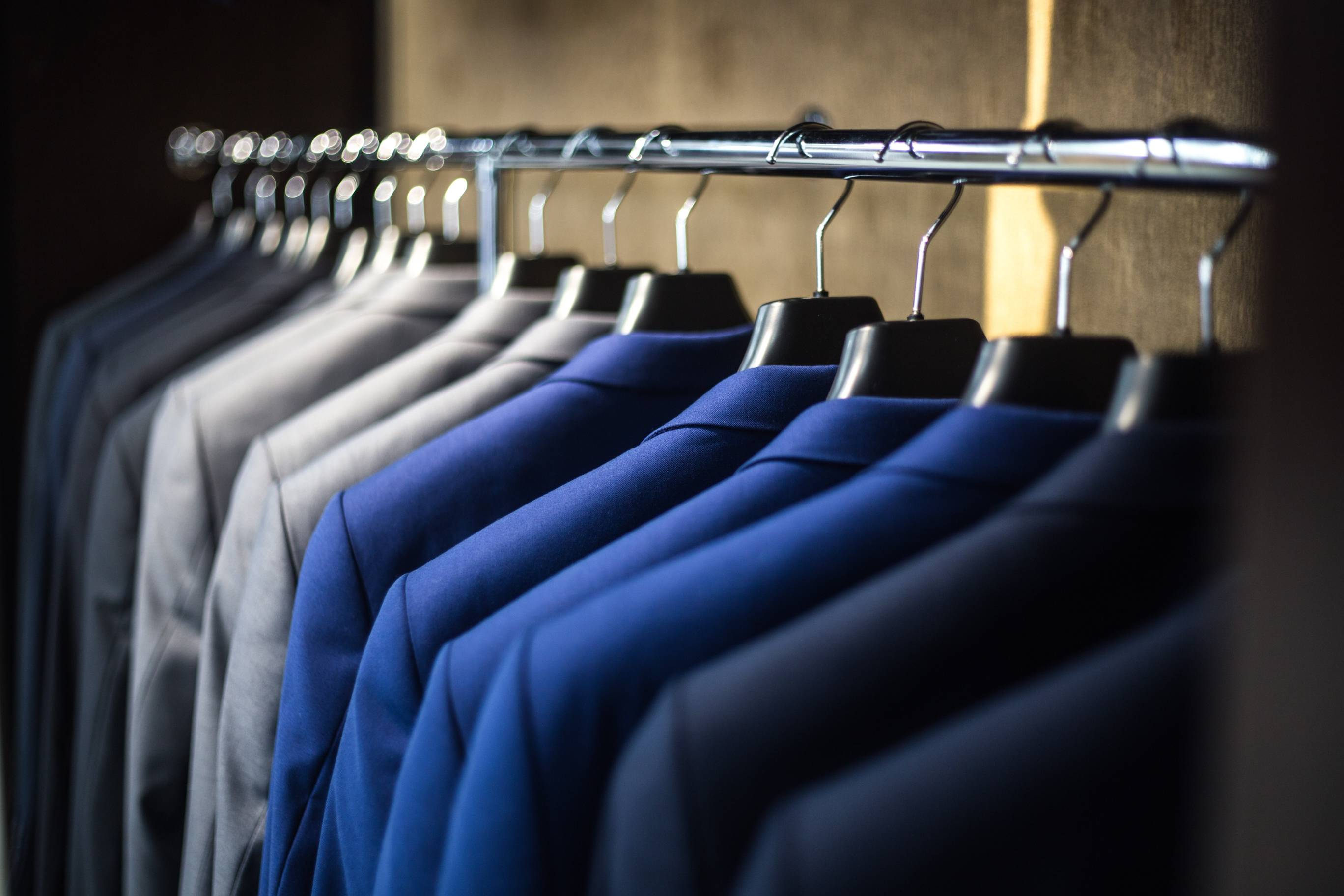 gray, blue and black suit jackets hanging from clothes hangers on a silver clothes rack