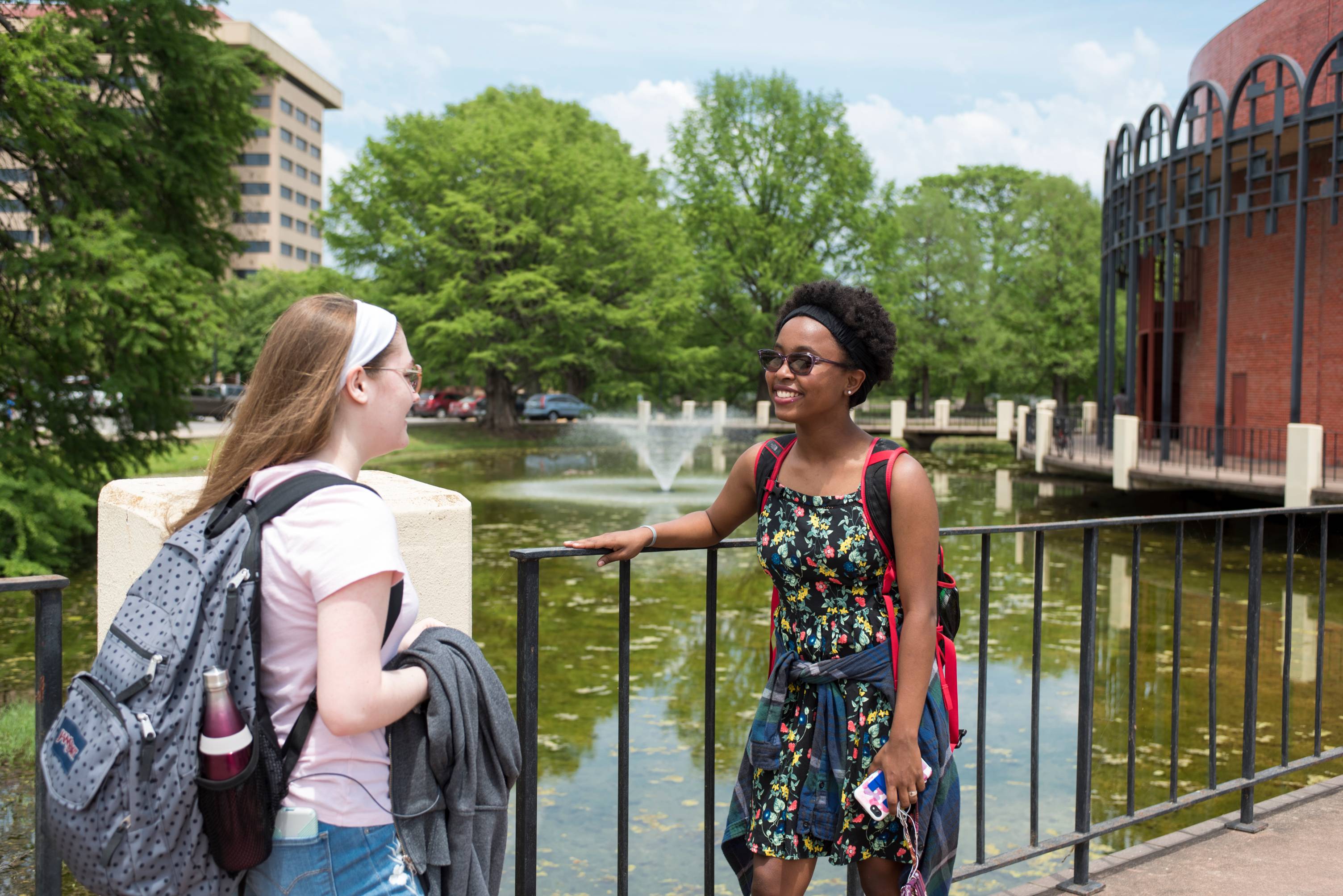 Two students talk besides the railing of the Theatre building.