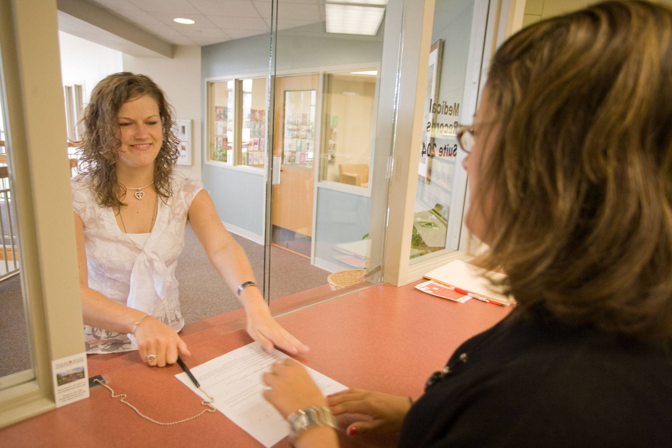 woman hands a form to another woman through a reception window