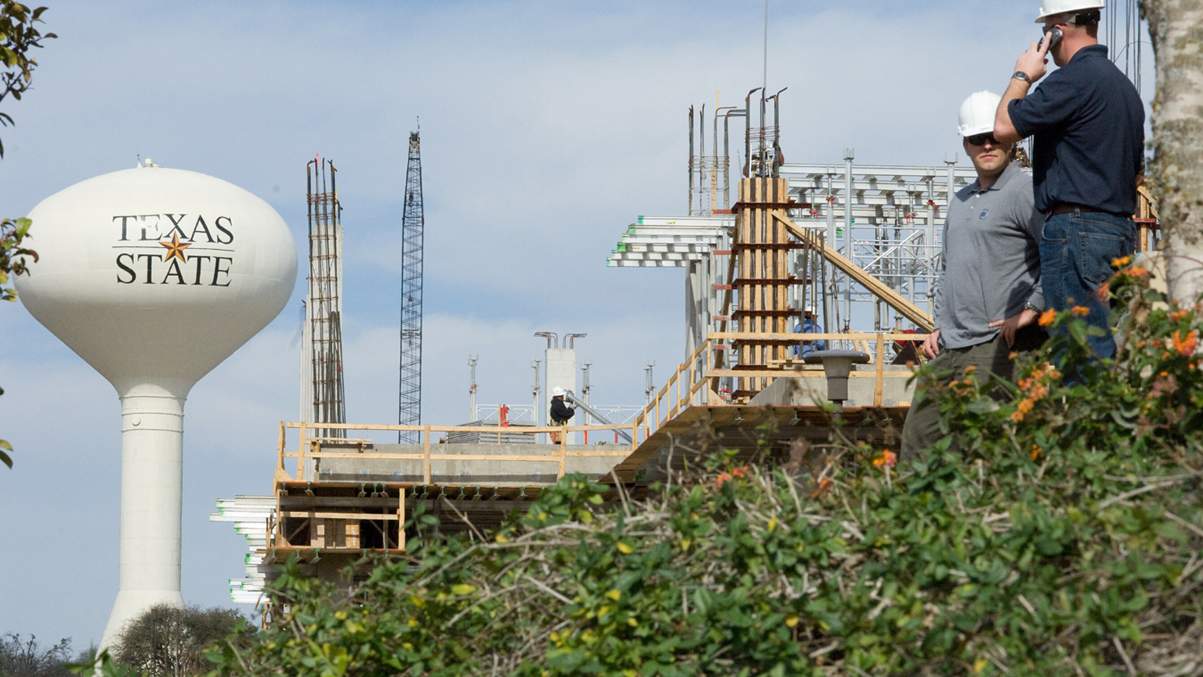 Foremen in the foreground, building in progress behind them, and a water tower in the distance.