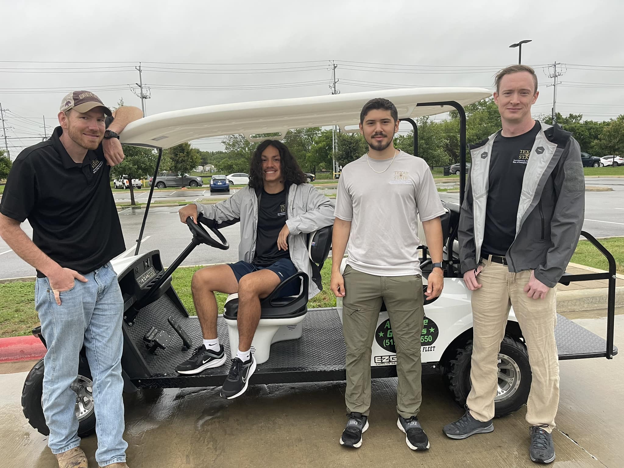 1 golf cart parked with 3 students and 1 staff member standing in front of it