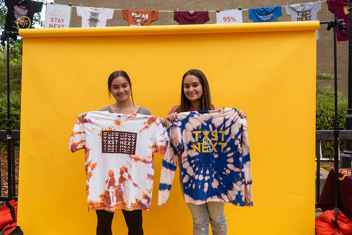 two woman holding up shirts in front of yellow backdrop