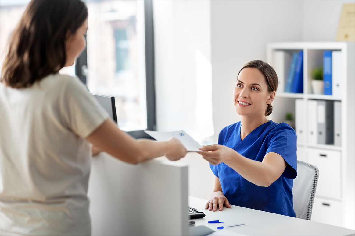 A female in slacks sitting behind a computer handing a woman a card.