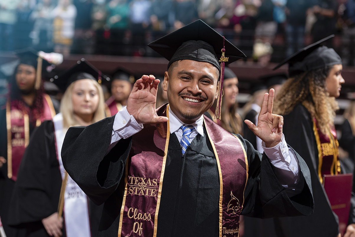 male graduate holding up txst hand signs