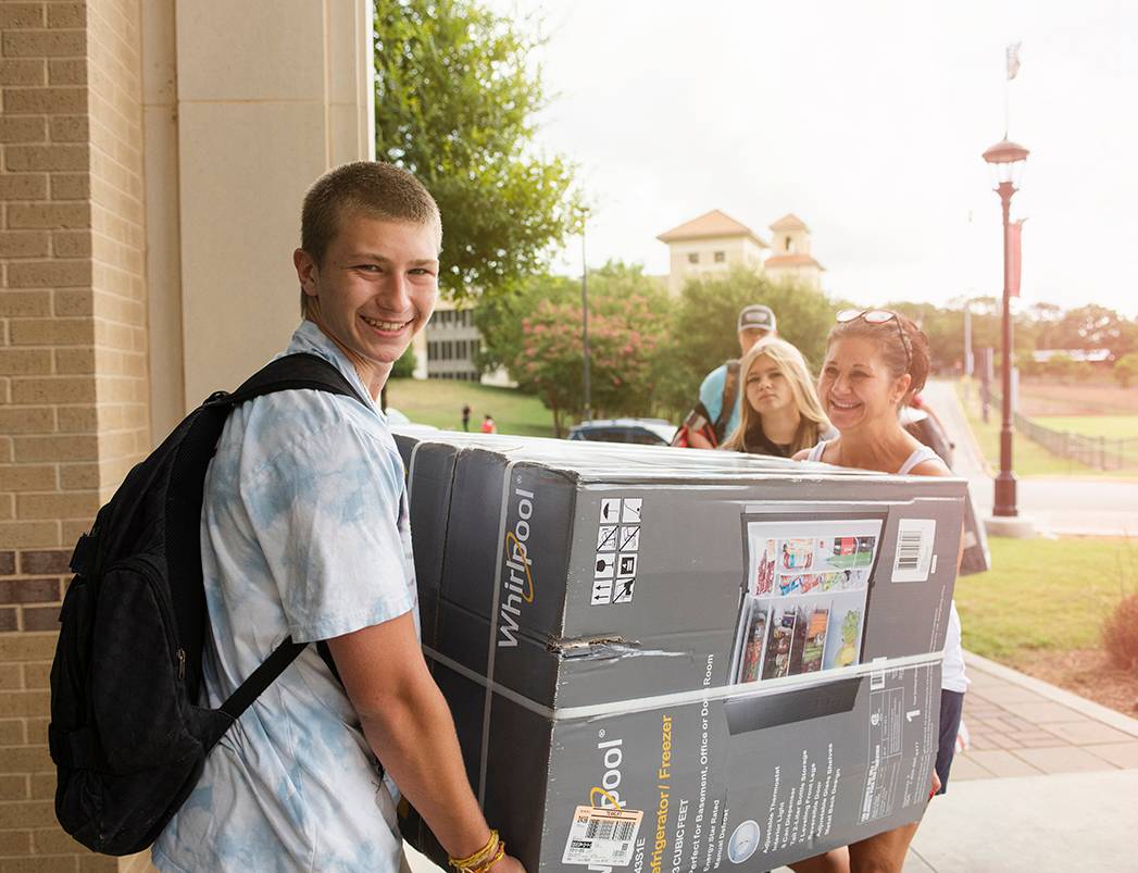 male student and mom carrying mini fridge on move-in day