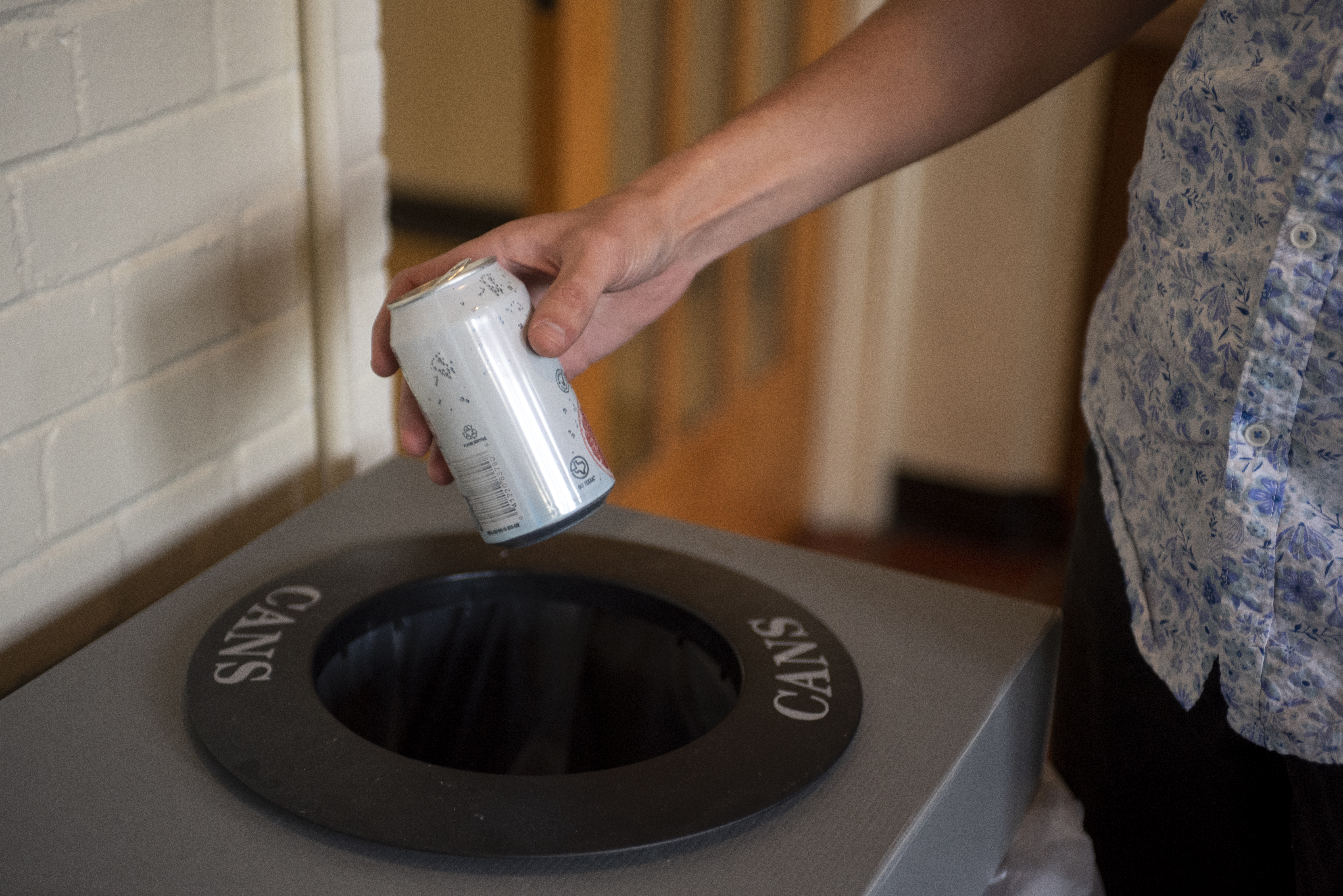 someone placing an aluminum can in a bin with "cans" written on it