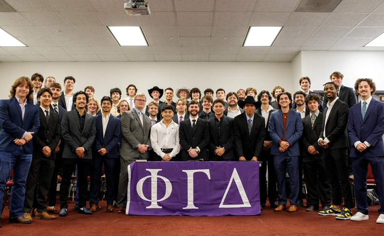 Men of Phi Gamma Delta (FIJI) stand behind a table and under a canopy while recruiting in the Quad