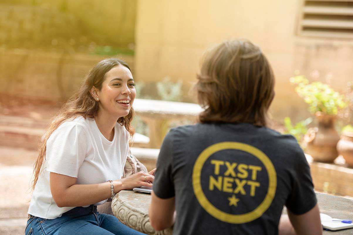 female student speaking to male student who is wearing a shirt reading 'txst next'