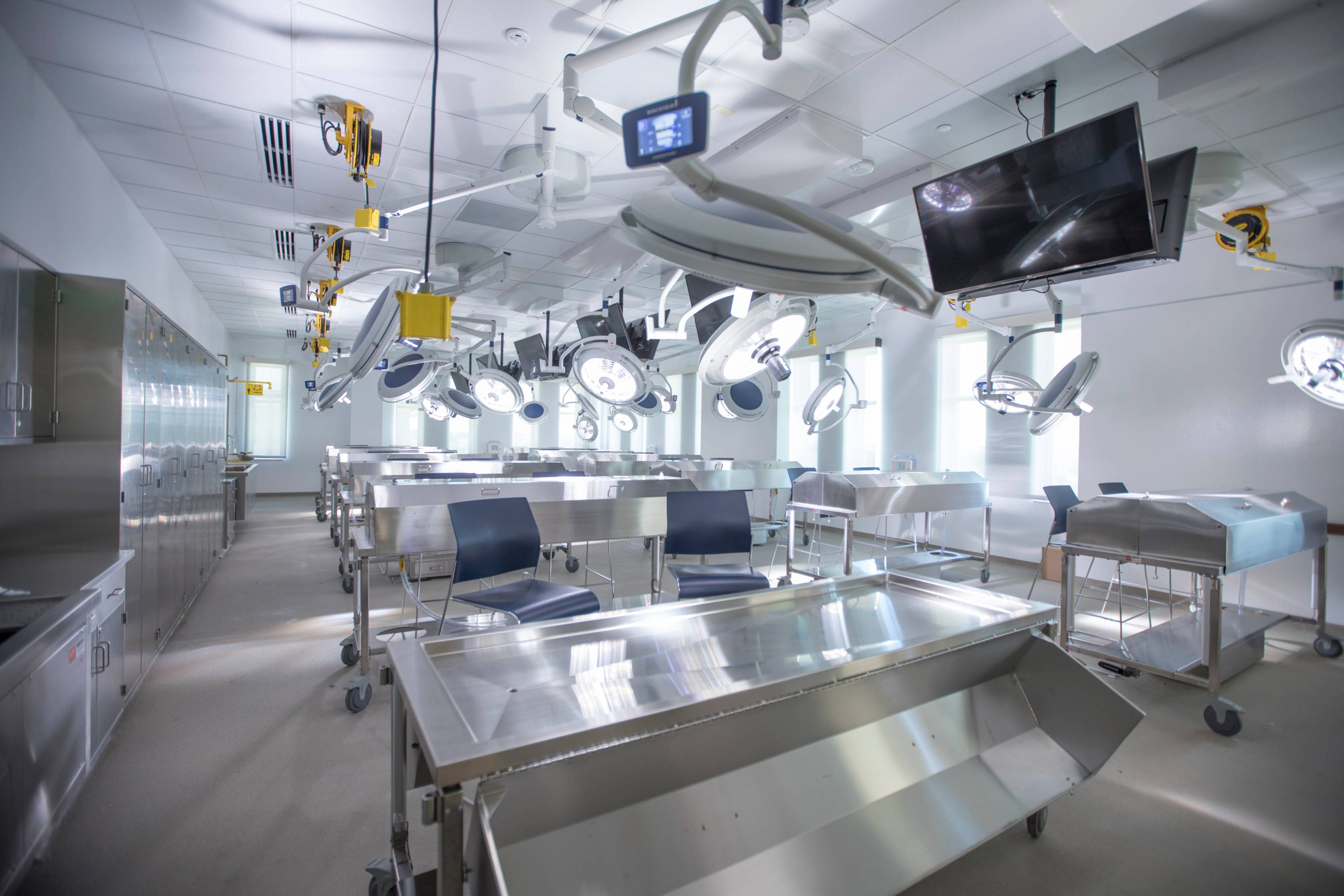 Anatomy lab on the Round Rock campus containing multiple stainless steel tables and bright, adjustable overhead lamps. 