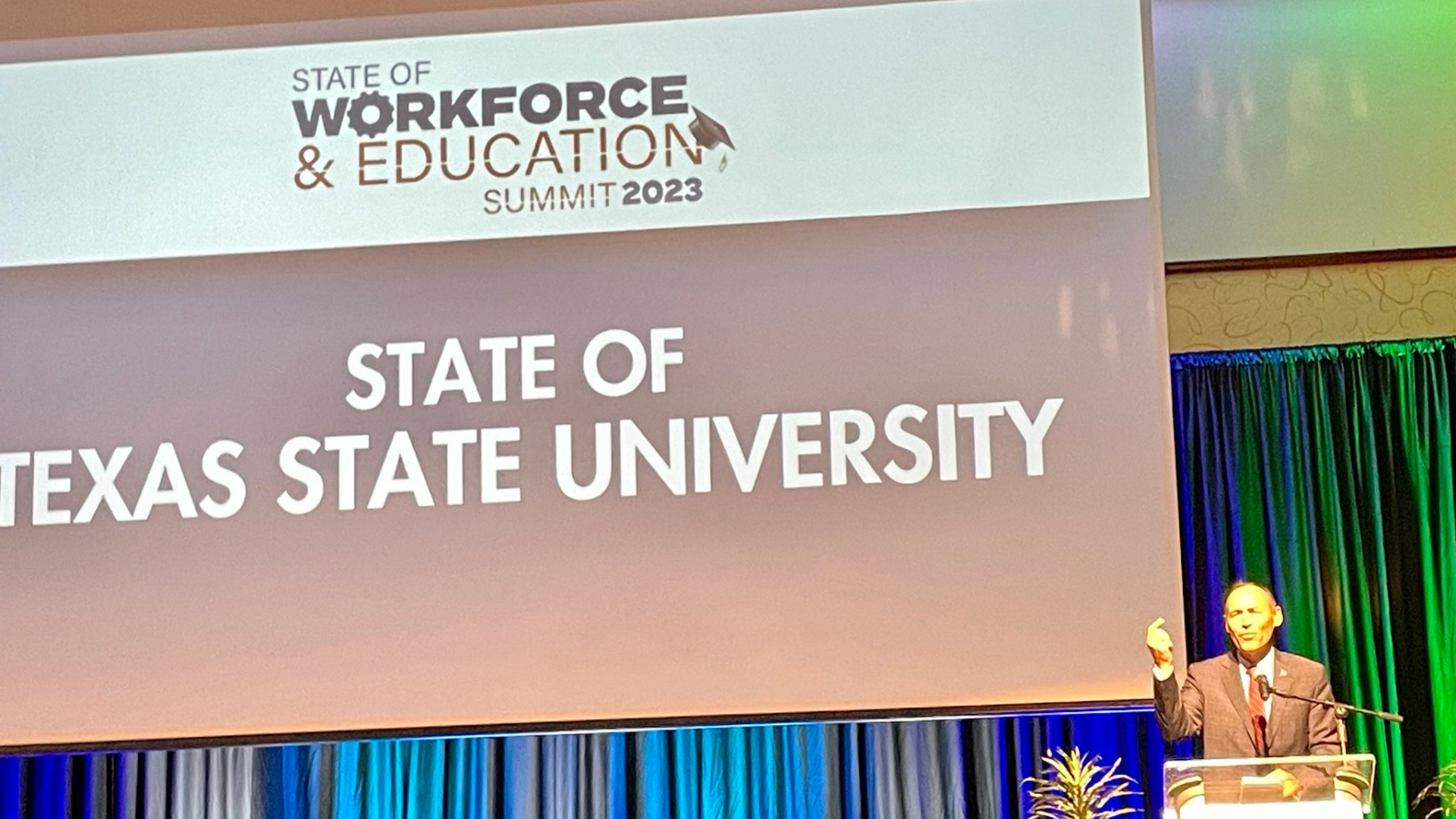President Damphousse stands a podium, speaking at the Education and Workforce Summit. 