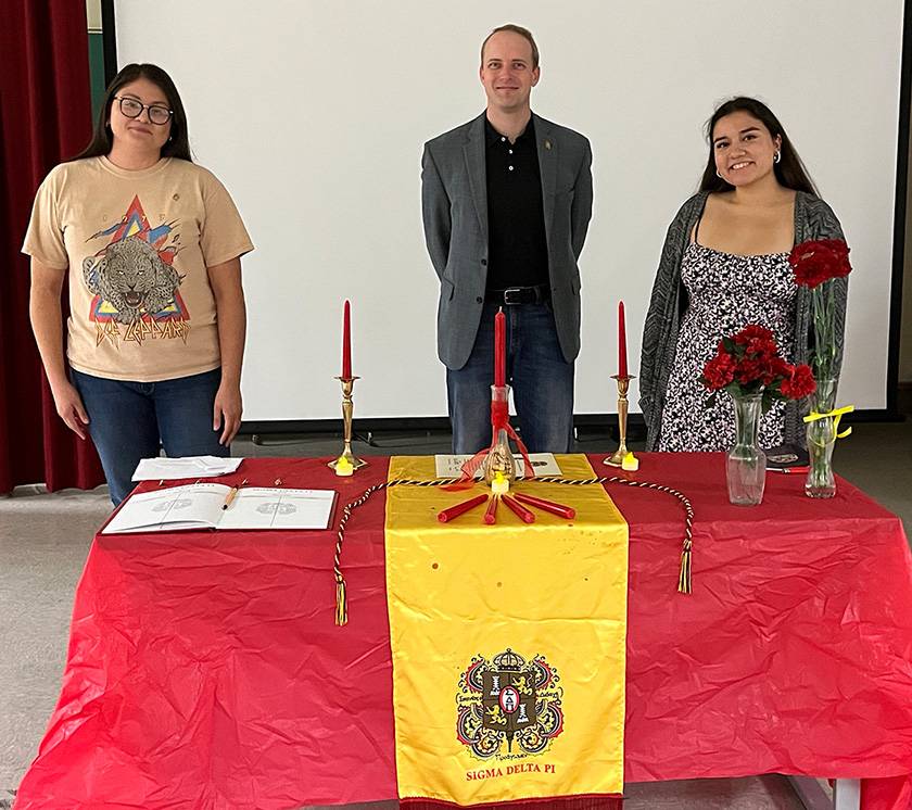 Three Sigma Delta Pi members posing for a photo behind a decorated table.