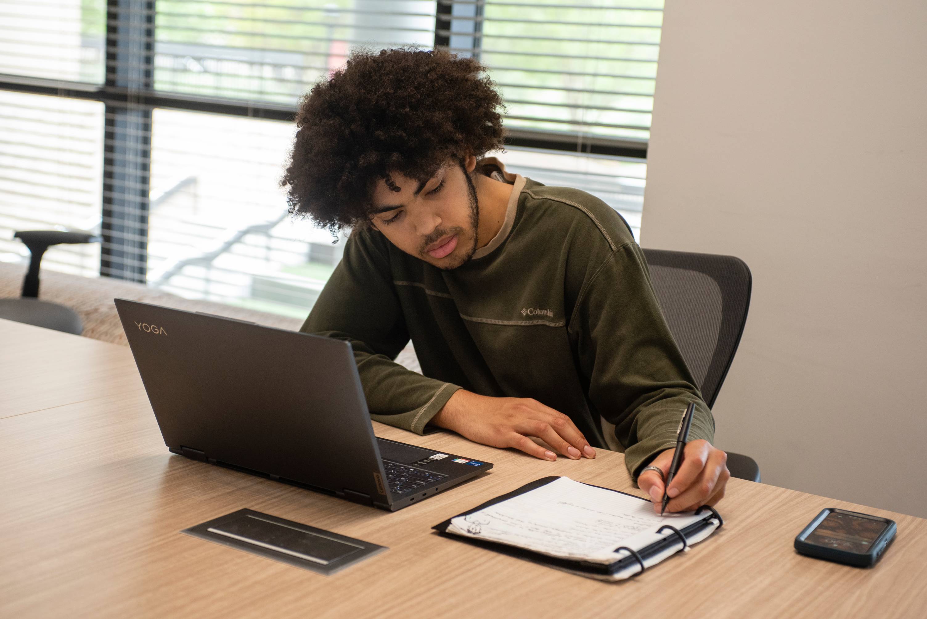 Student writing in notebook with their laptop open in front of them