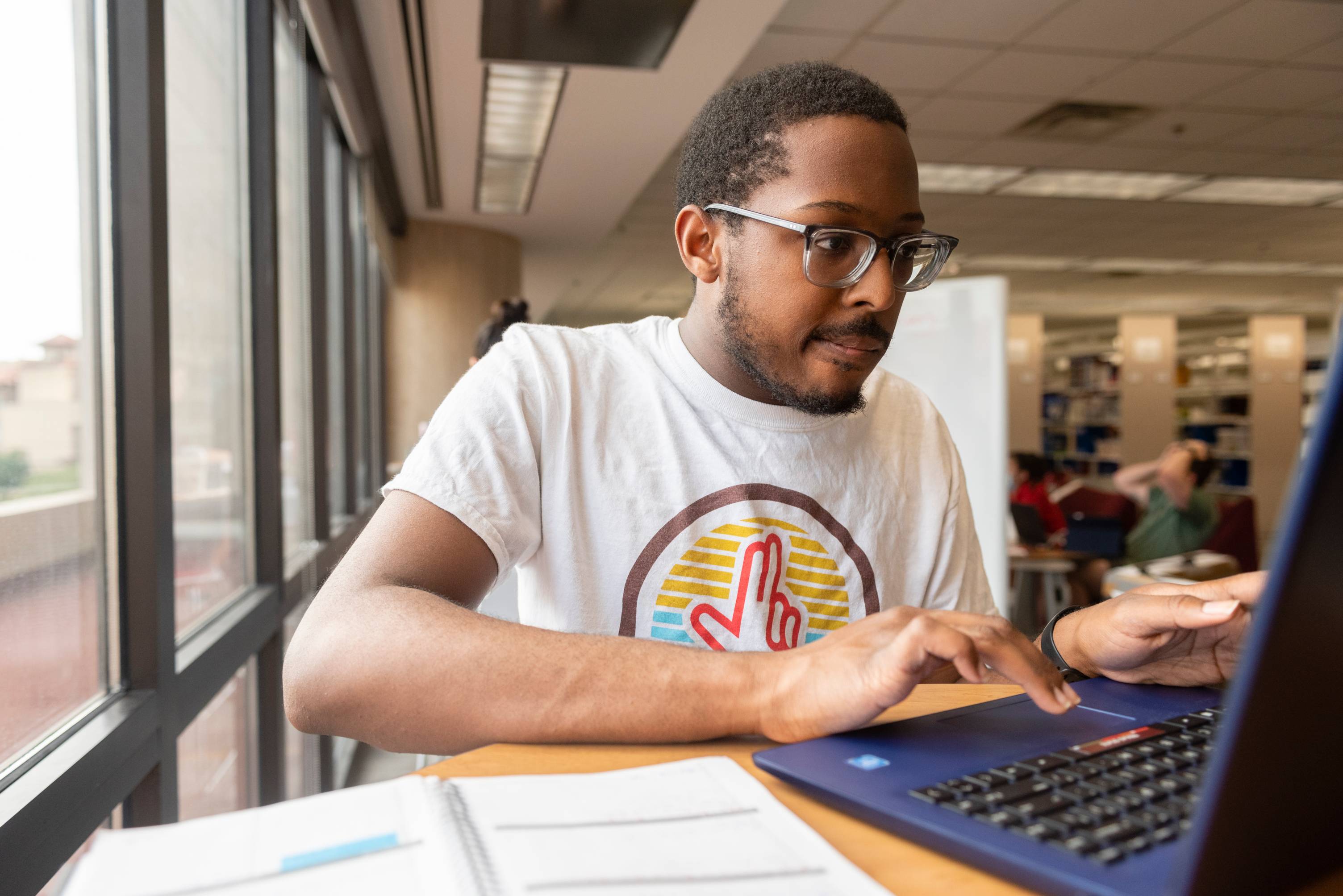 Student working on laptop in the Alkek Library next to a window with an open planner nearby