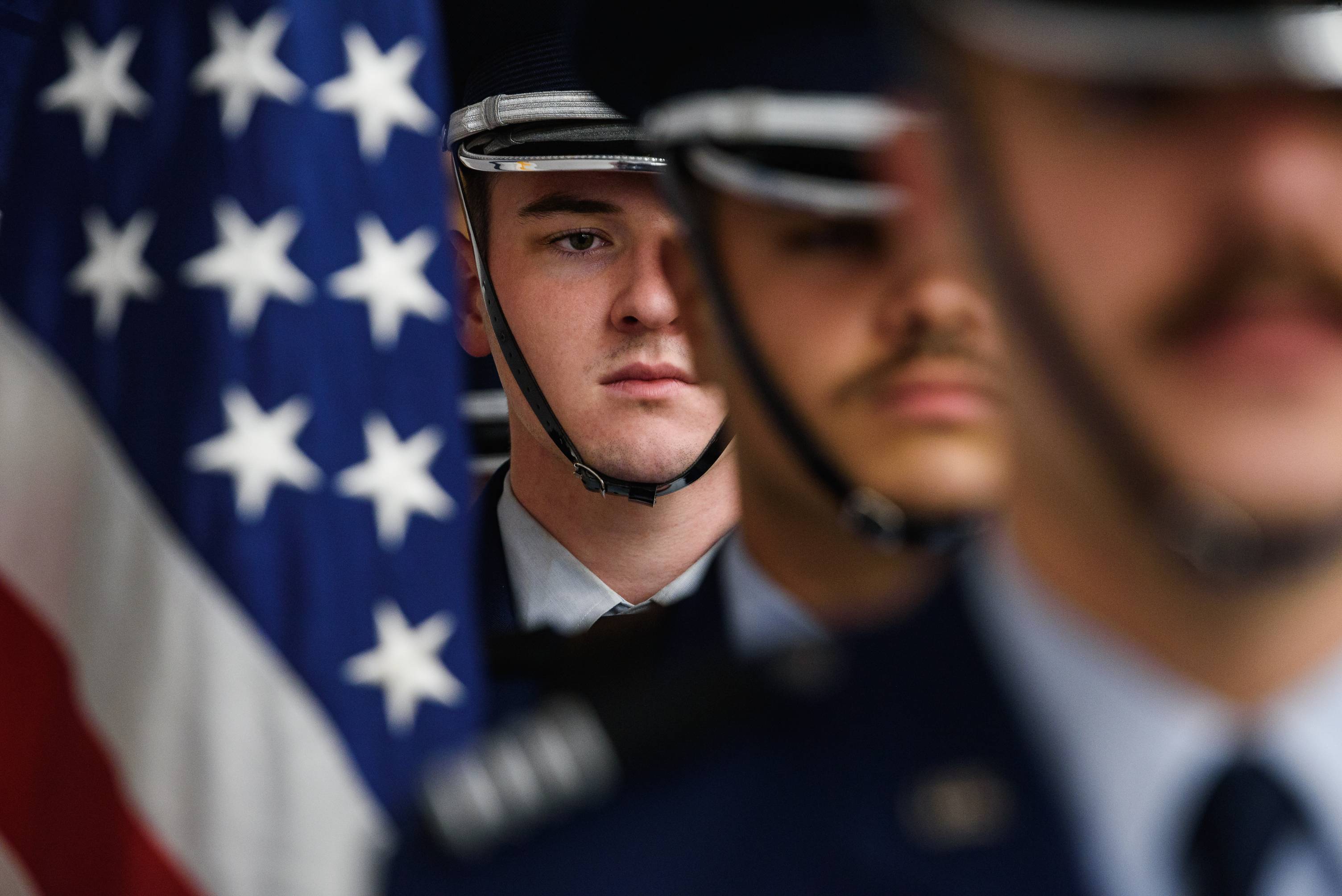 Three uniformed officers standing solemn-faced with the American flag hanging next to them