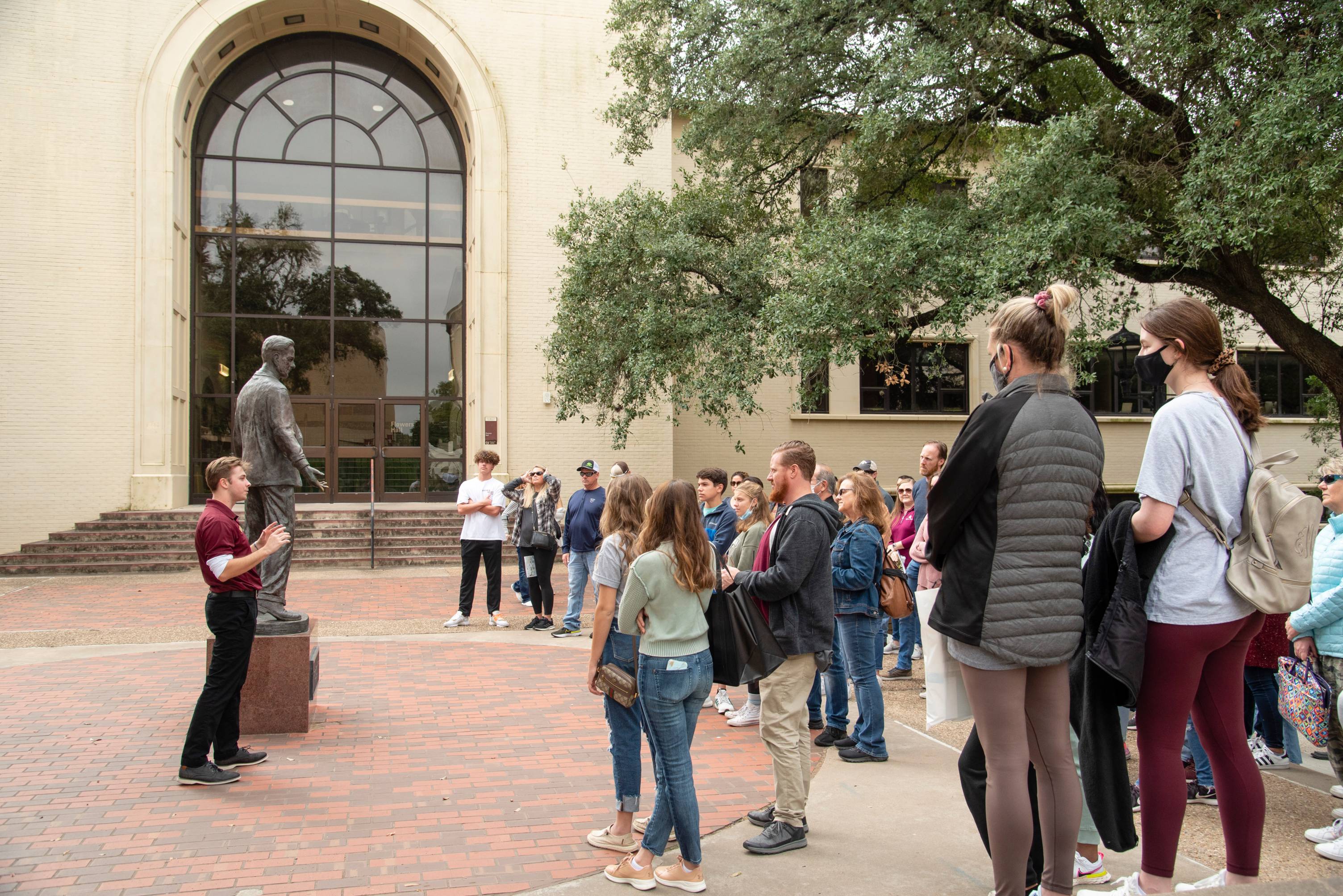 Tour guide standing next to the LBJ statue speaking to large group of individuals in front of Flowers Hall