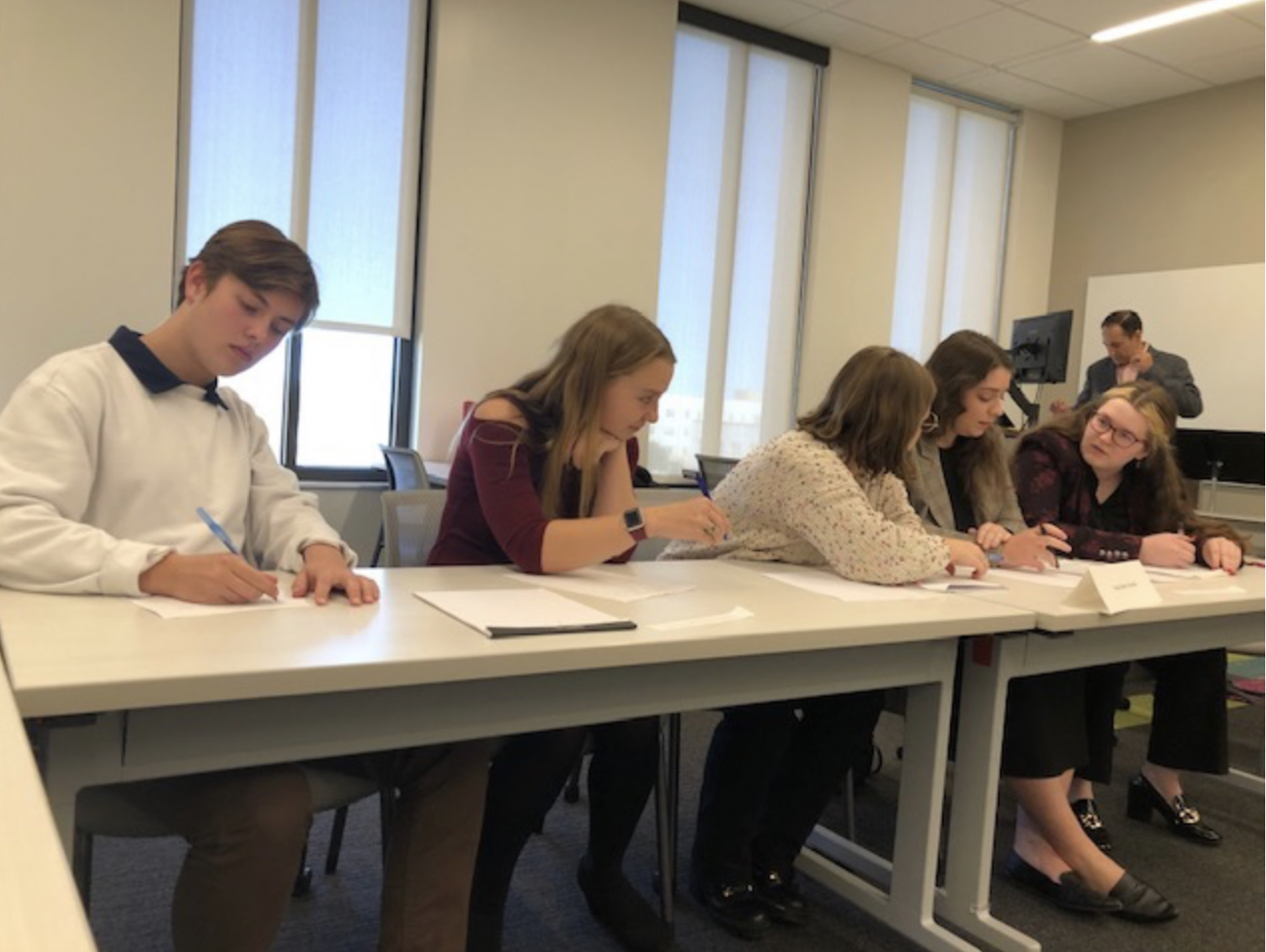students sitting at a long desk talking and writing
