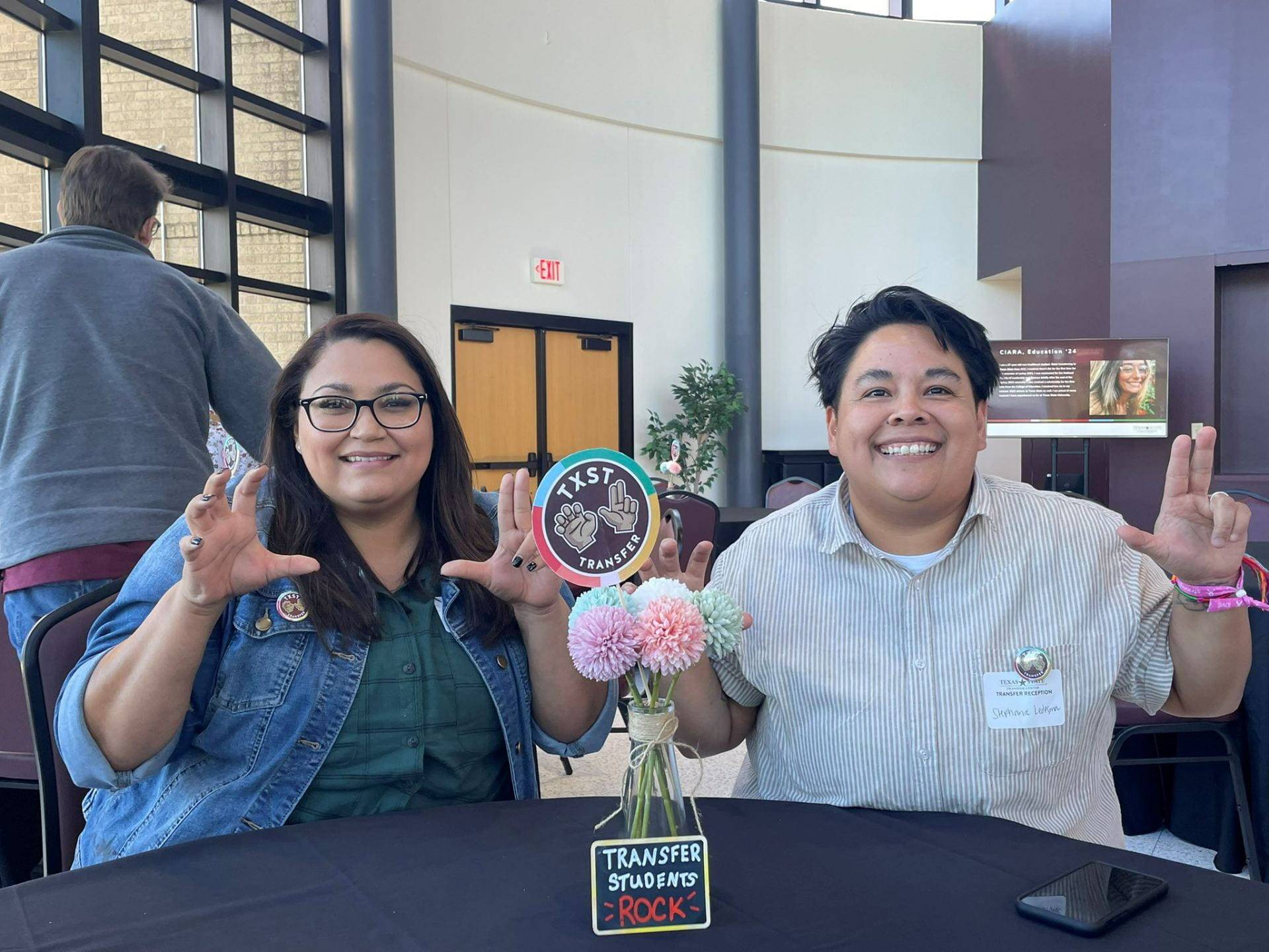 two students do the TXST hand sign with a Transfer Center sign in front of them