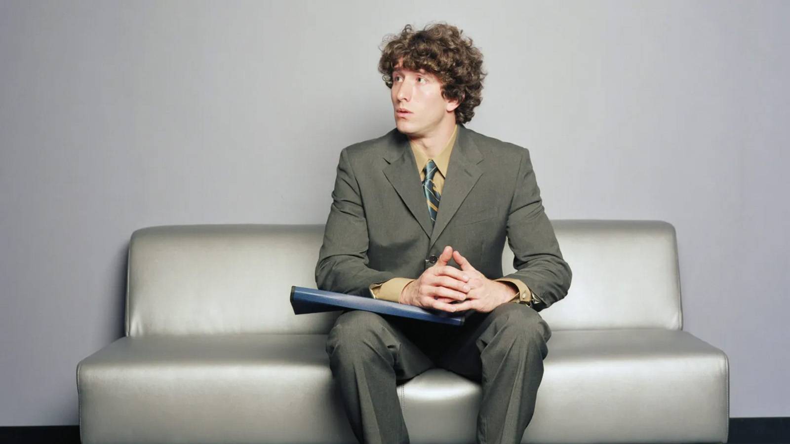Young businessman in suit seated on couch awaiting interview