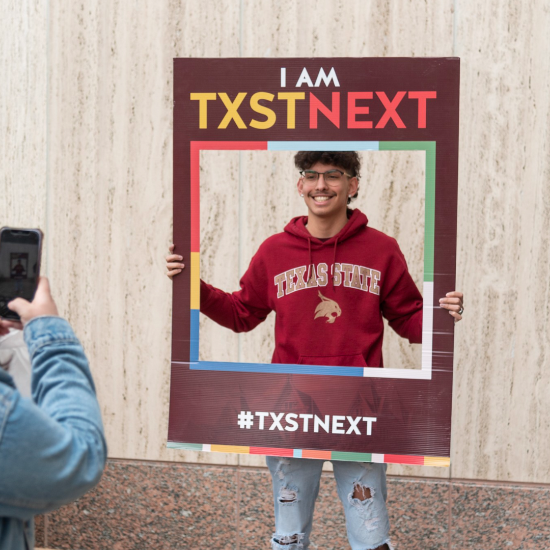 Student holding frame for photo with I AM TXST NEXT written on it at Bobcat Day