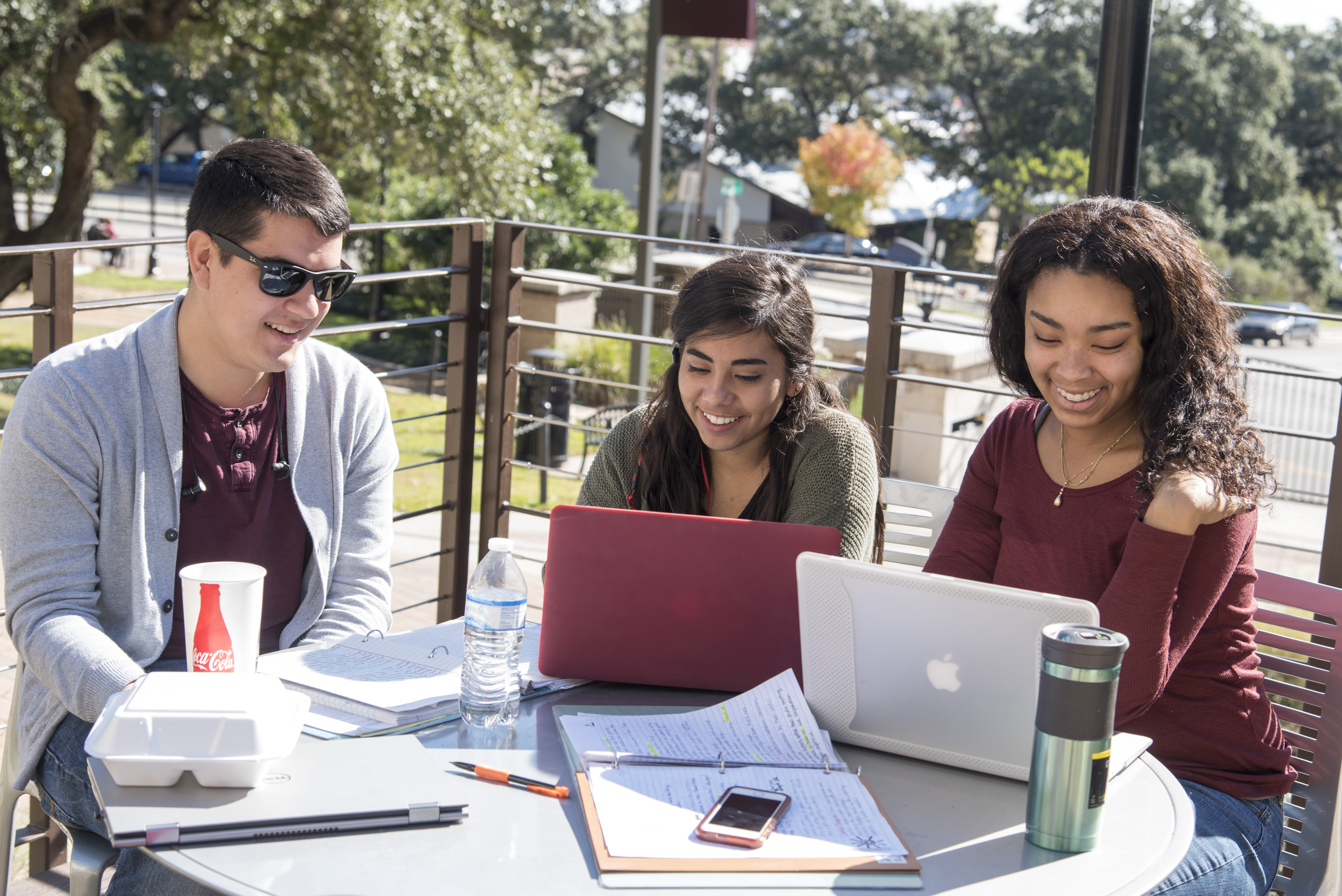 three students working on laptops outside with sun beating down