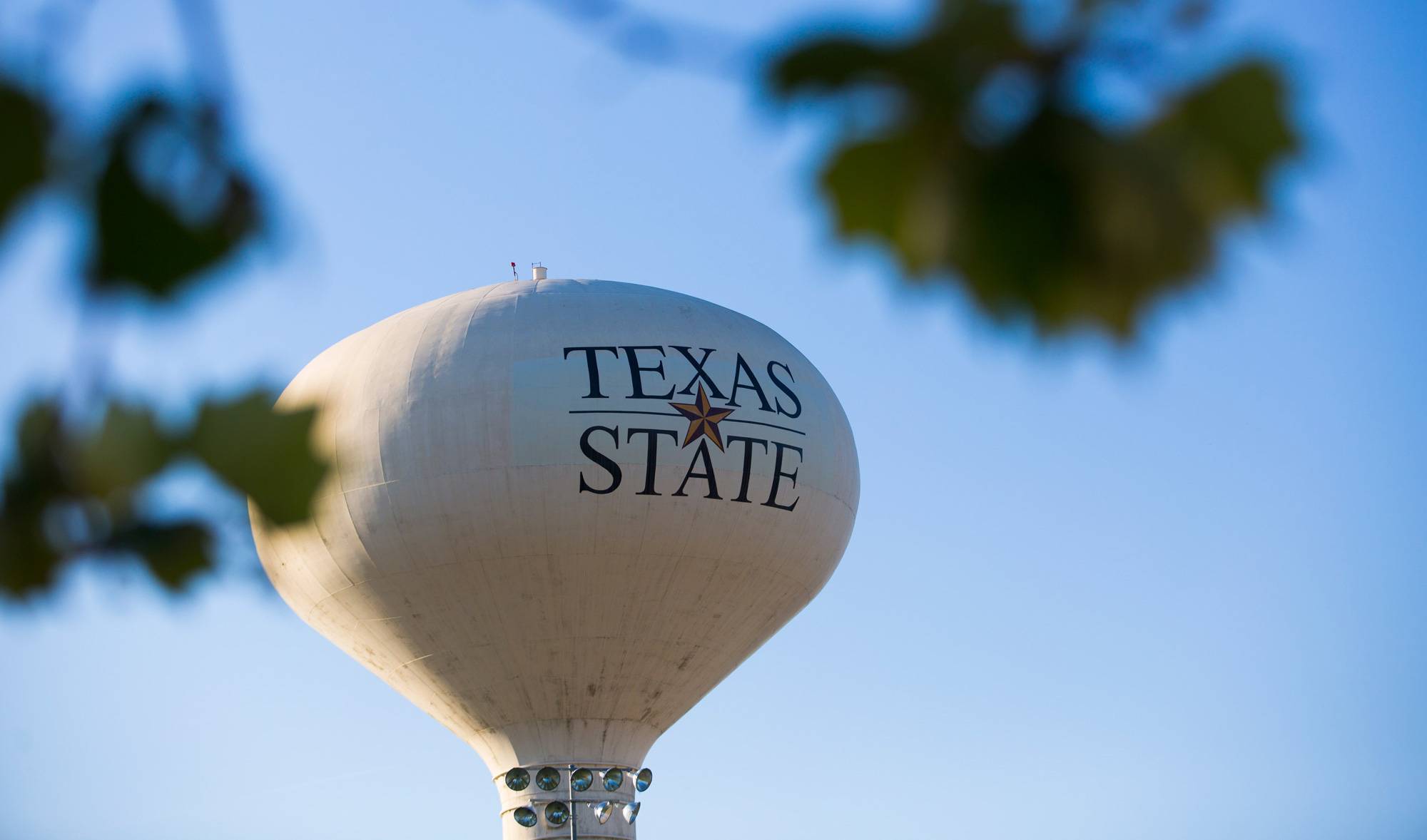 Texas State University's water tower in the distance behind trees