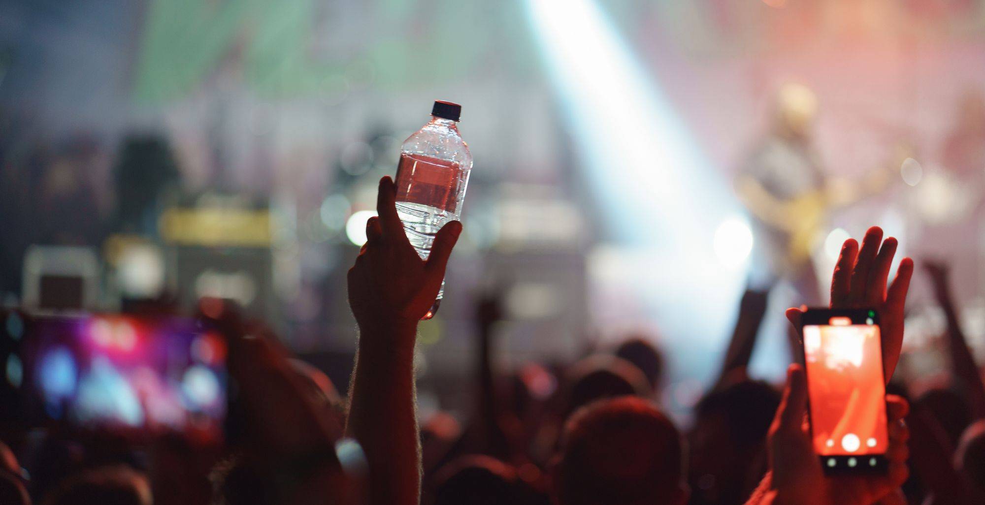 A closeup of a hand holding up a water bottle in a busy crowd at a concert.