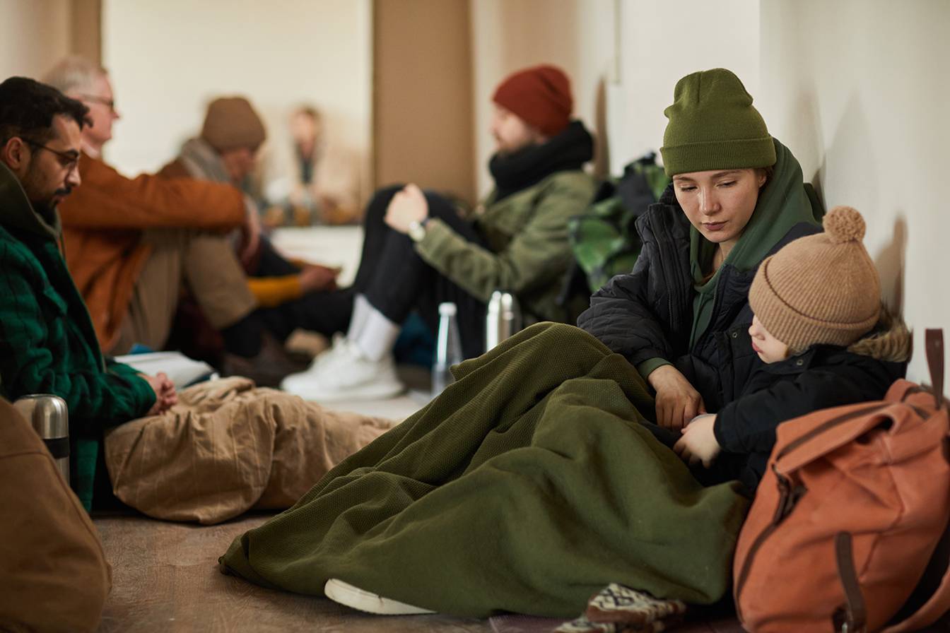 refugees sitting on floor covered in blankets 
