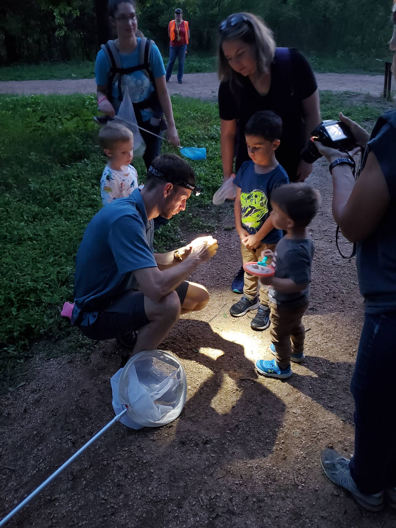 man with headlamp shows something in his hands to small children