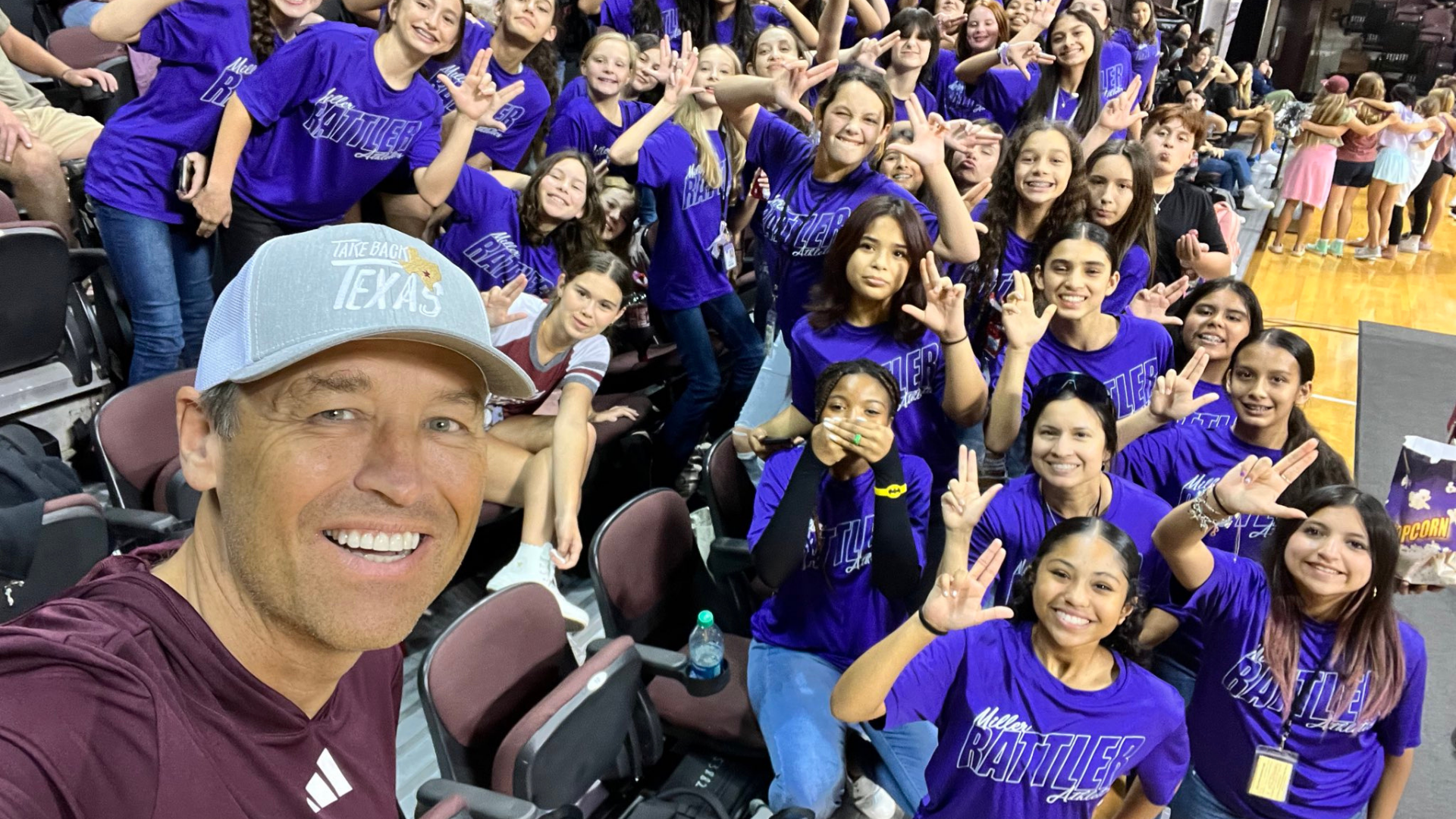 President Damphousse posing with a group of San Marcos middle school students at a Texas State University women's volleyball game.