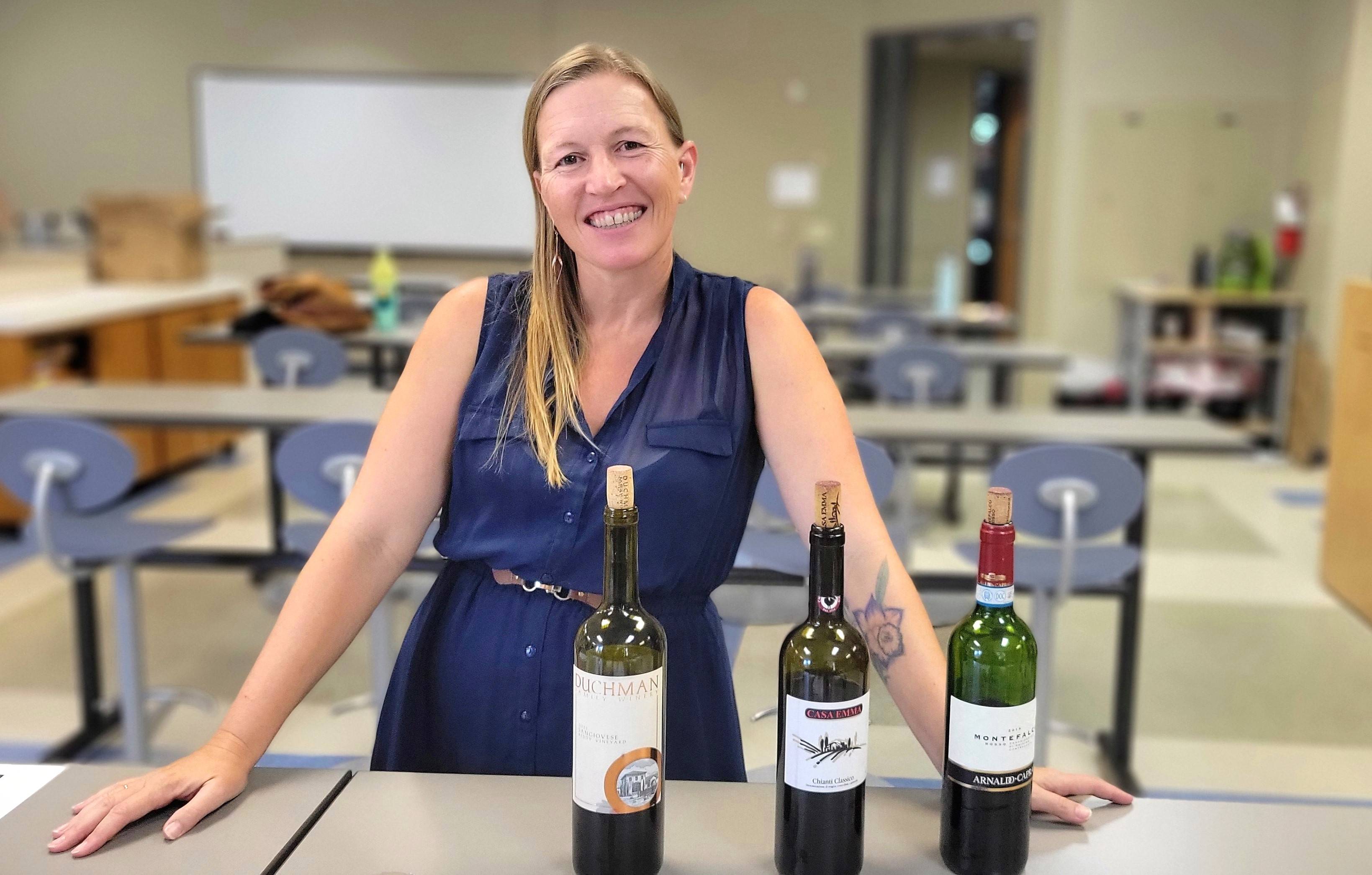 Image of Dr. Colleen Myles smiling in front of a table with three wine bottles at a didactic tasting.