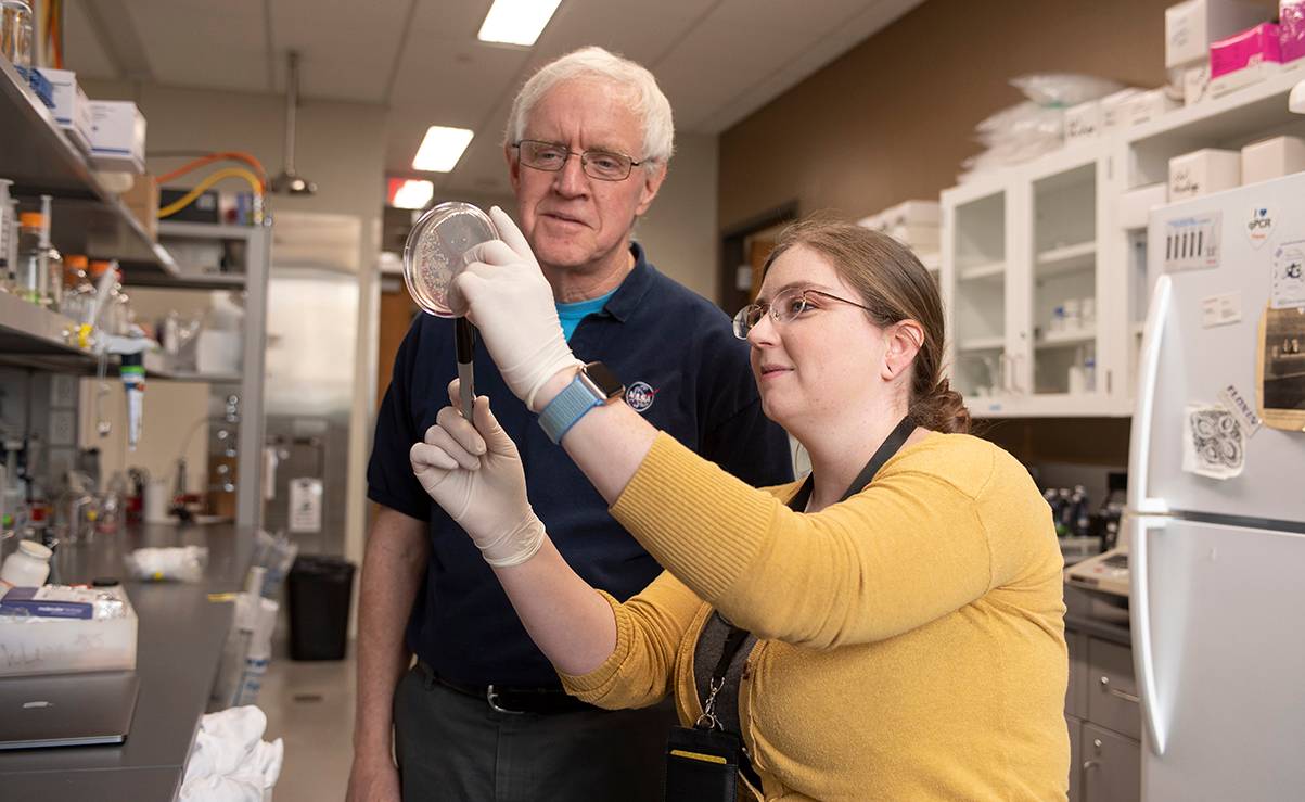 woman holding up petri dish for male faculty member to see