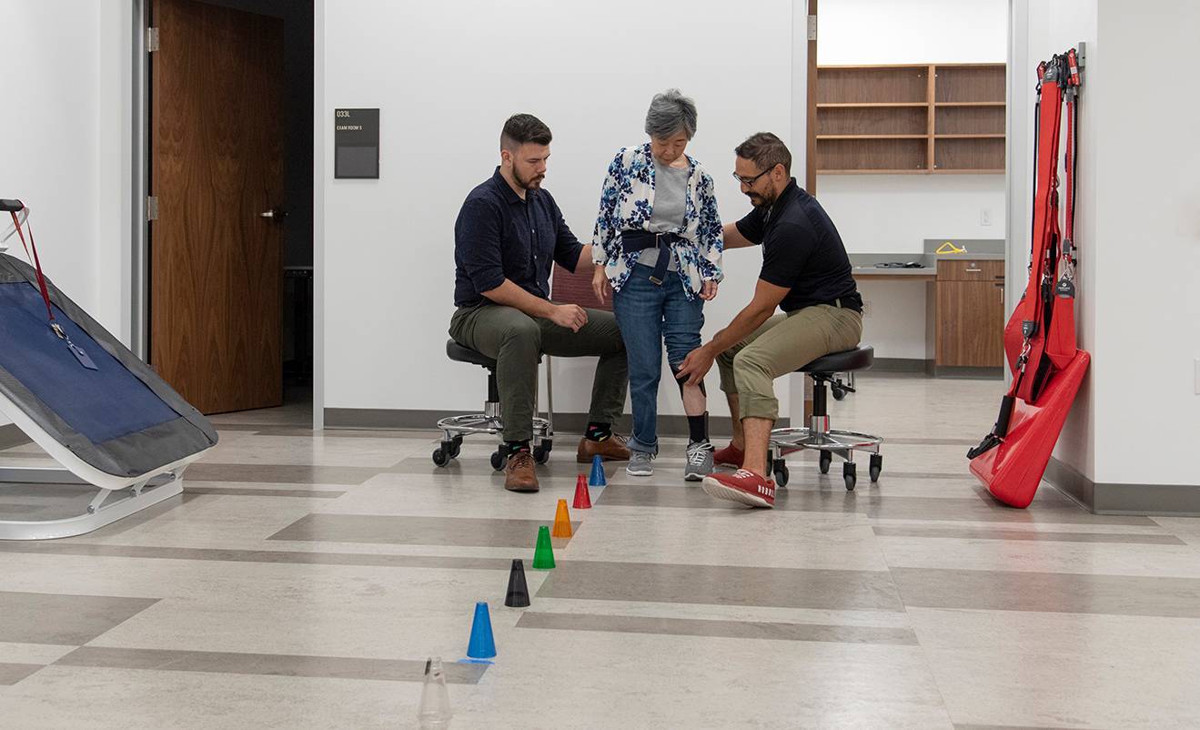 two men helping a woman in physical therapy exercises