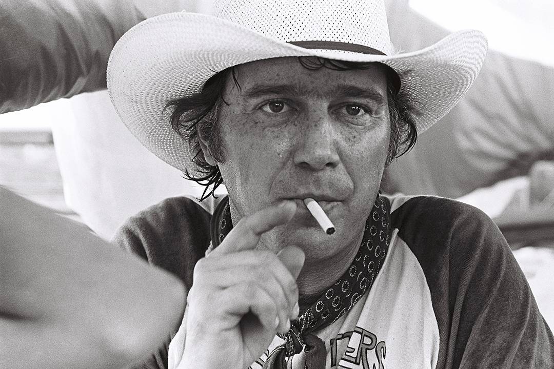 black and white photo of man in cowboy hat smoking cigarette