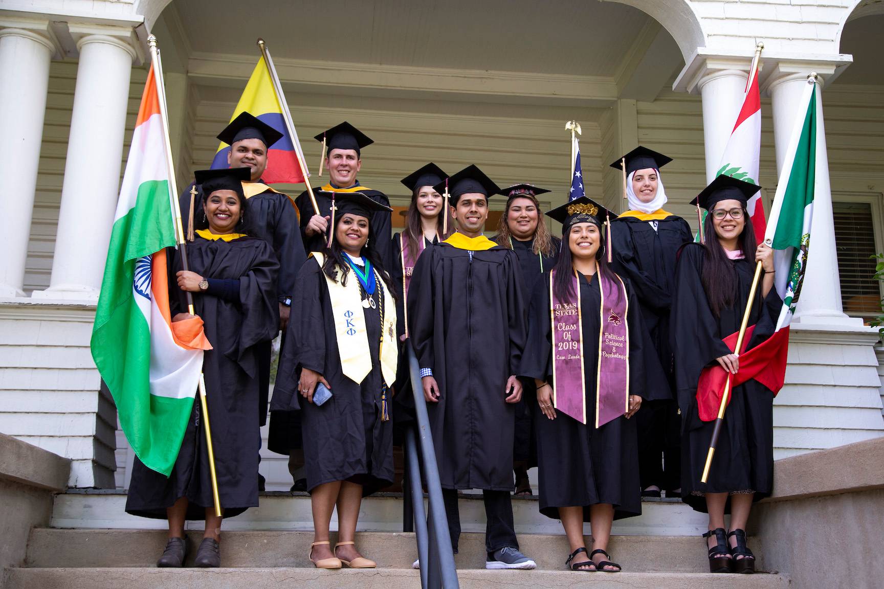 Group of international graduates dressed in regalia and waving their home country flag