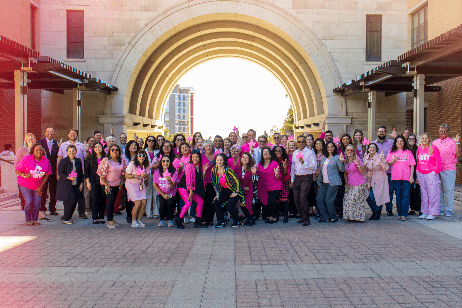 A group of employees posing in front of the Arch in pink.